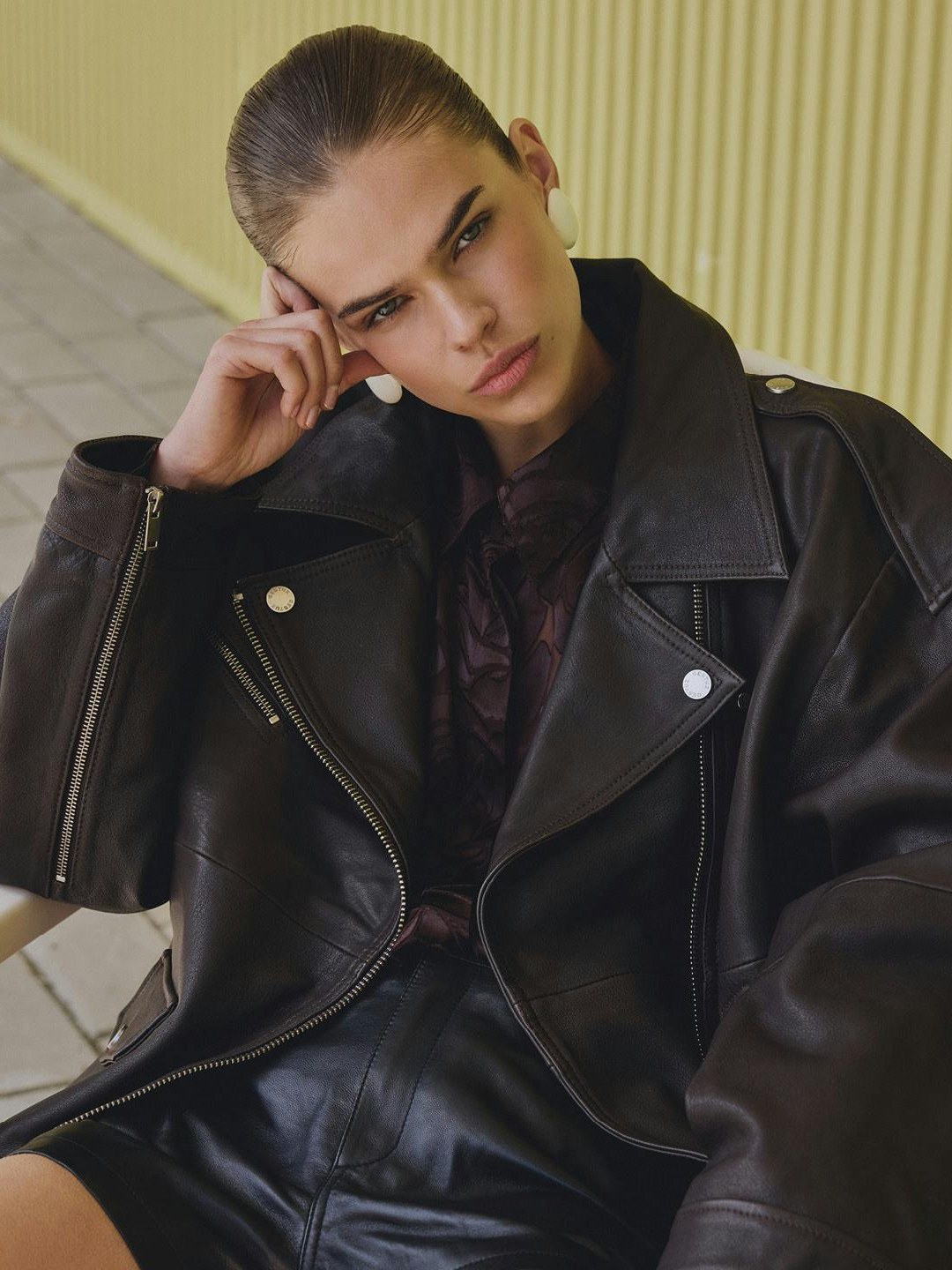 Model reclining in a dark leather jacket and skirt