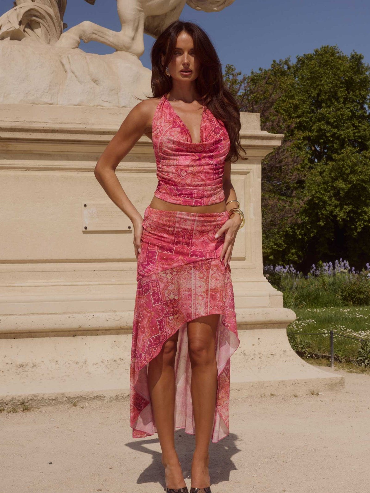 Model in a pink patterned sleeveless dress beside a pale stone terrace