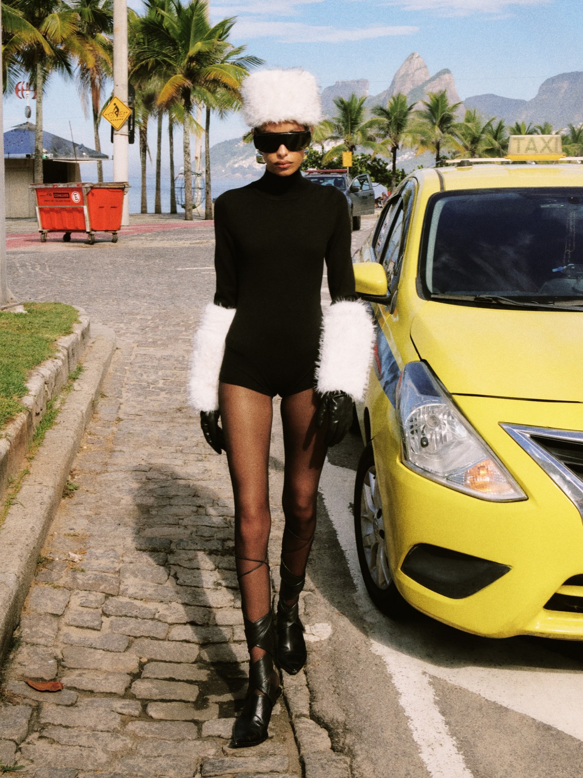 Model in a black outfit with white faux-fur accessories beside a yellow car