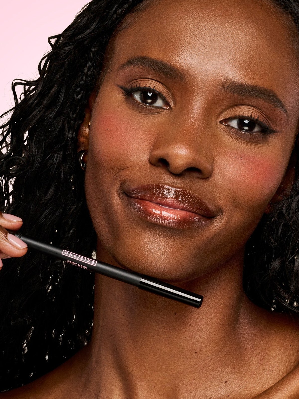 Model with long curly hair holding an eyeliner pencil at her chin