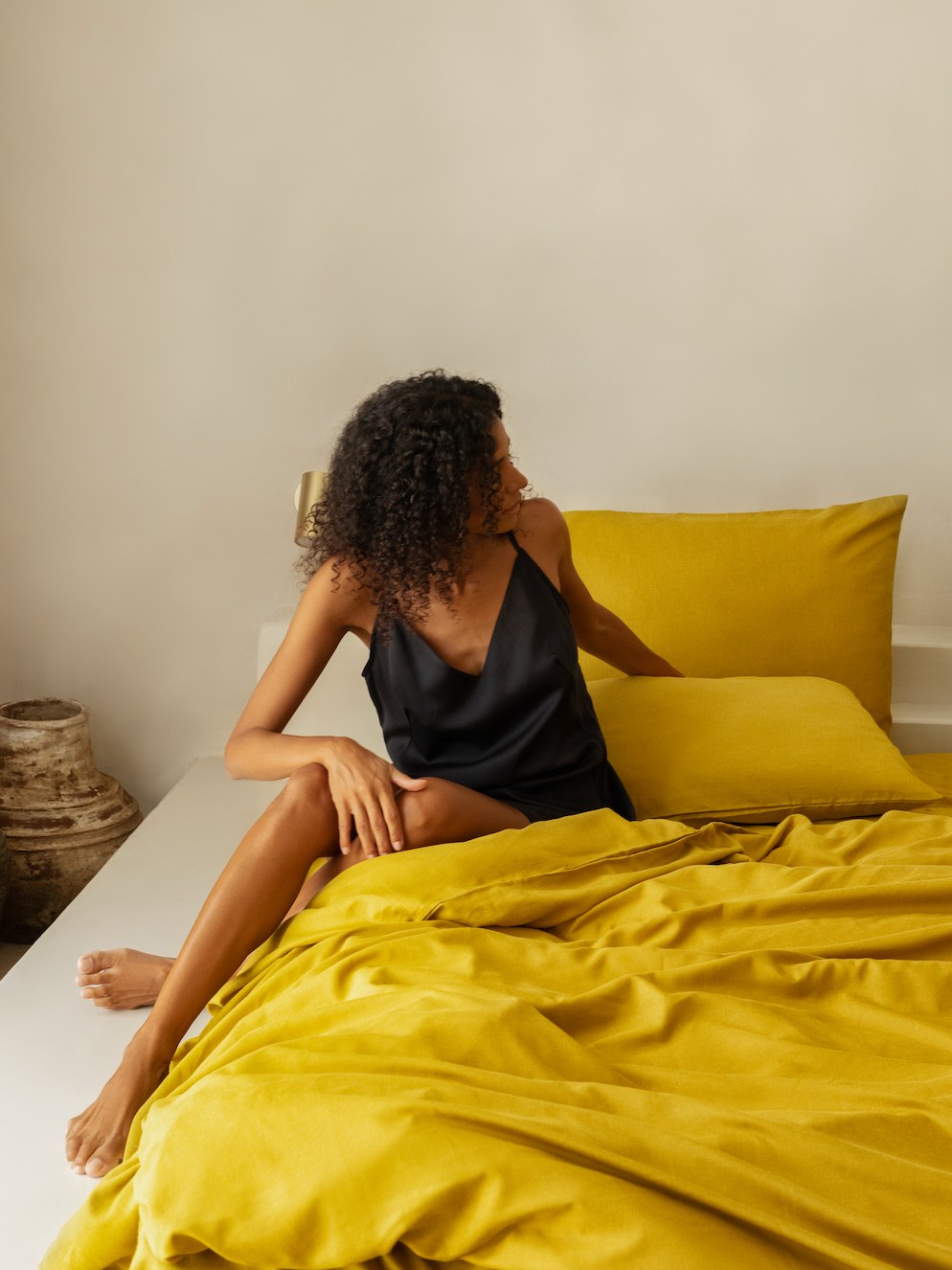 Woman seated on saffron bedding in a styled bedroom