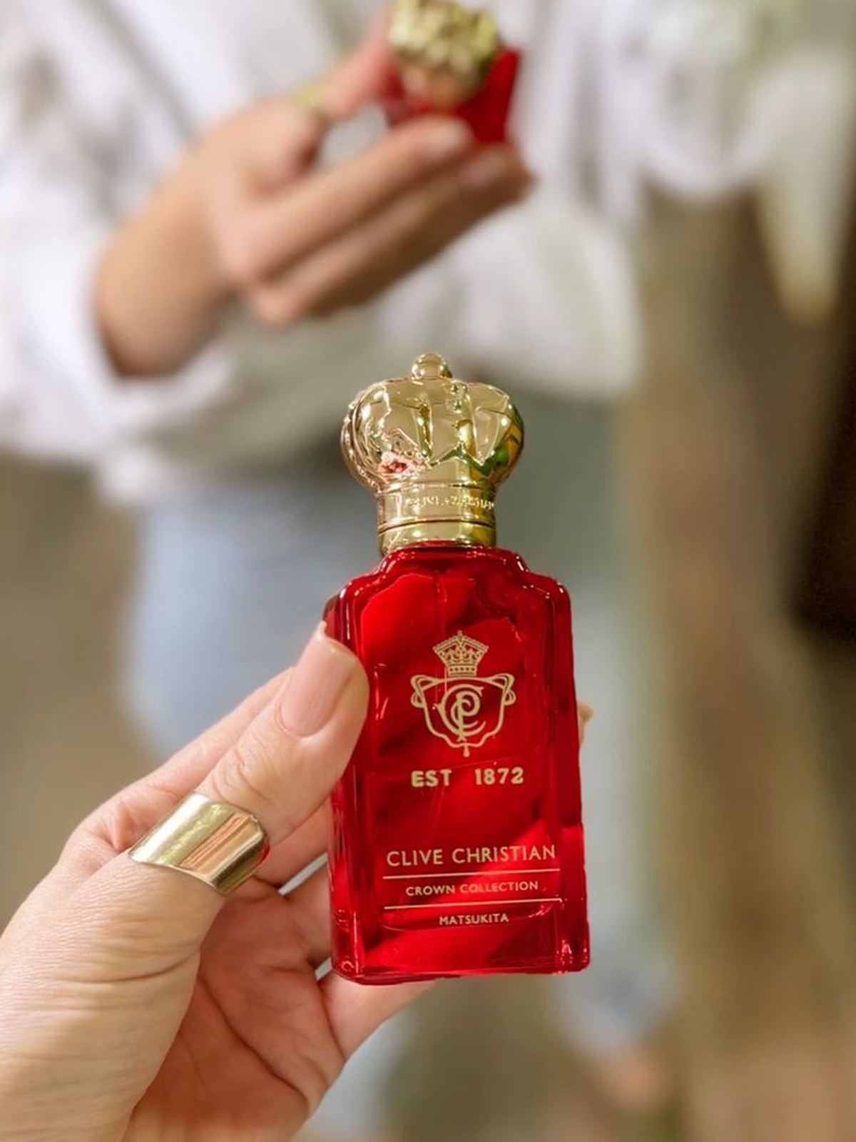 Hand holding a small red Clive Christian crown bottle outdoors
