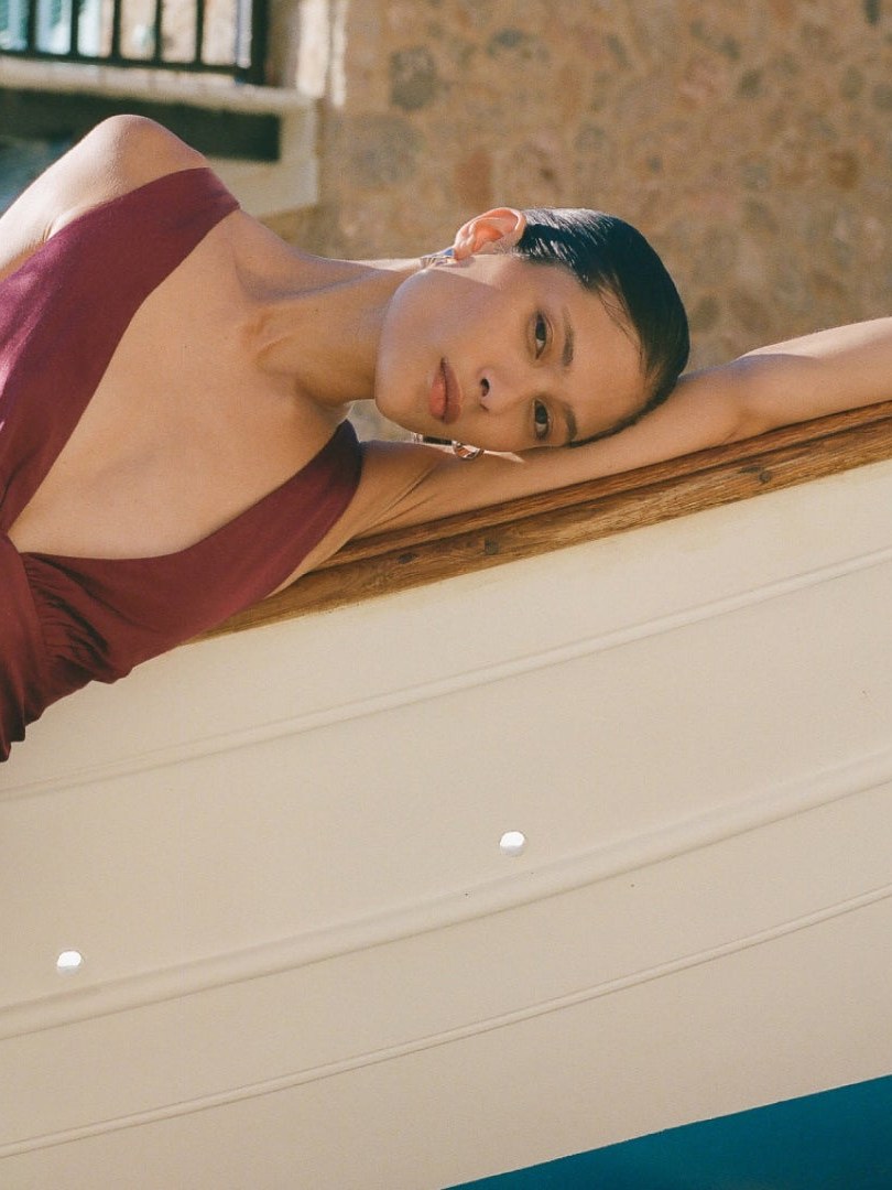 Model in a plum dress reclining along a boat