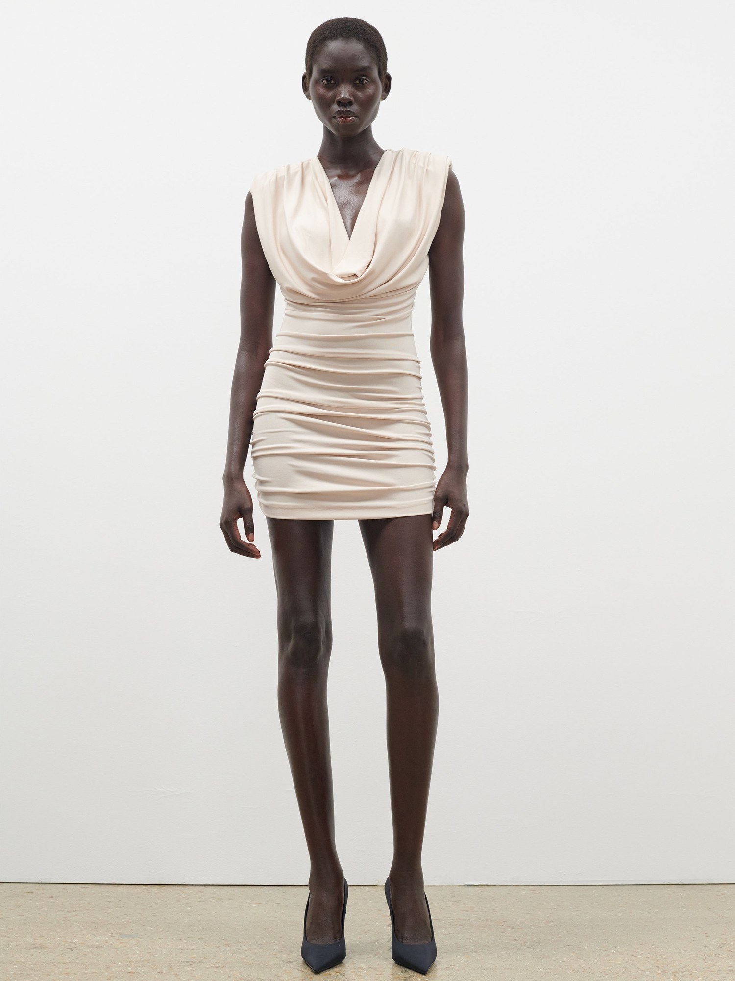 Model in a cream draped sleeveless mini dress and black heels