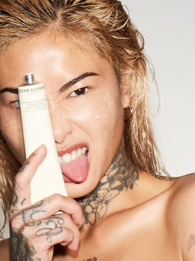 Model holding a Grown Alchemist skincare tube beside her eye in a playful studio portrait