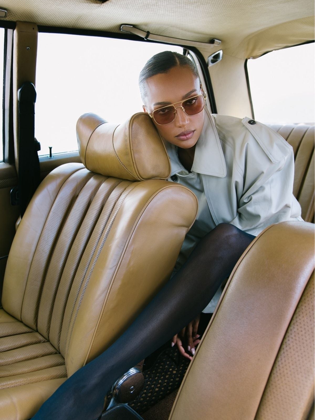 Model in sunglasses reclining in the back of a car in cream outerwear
