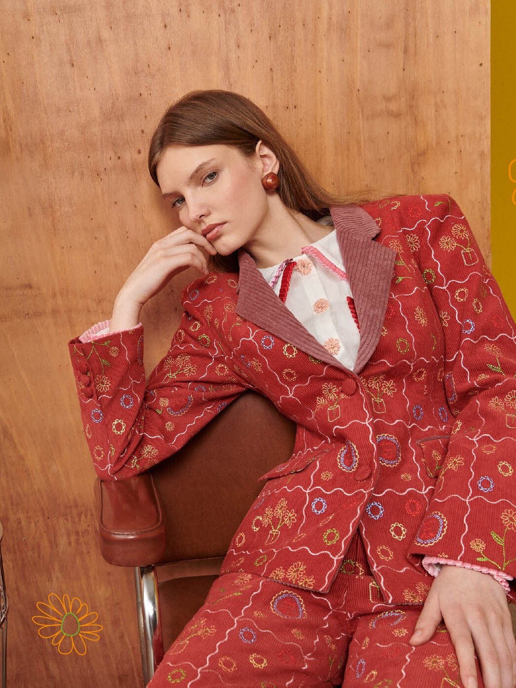 Woman seated in a patterned red suit in a warm illustrated studio set