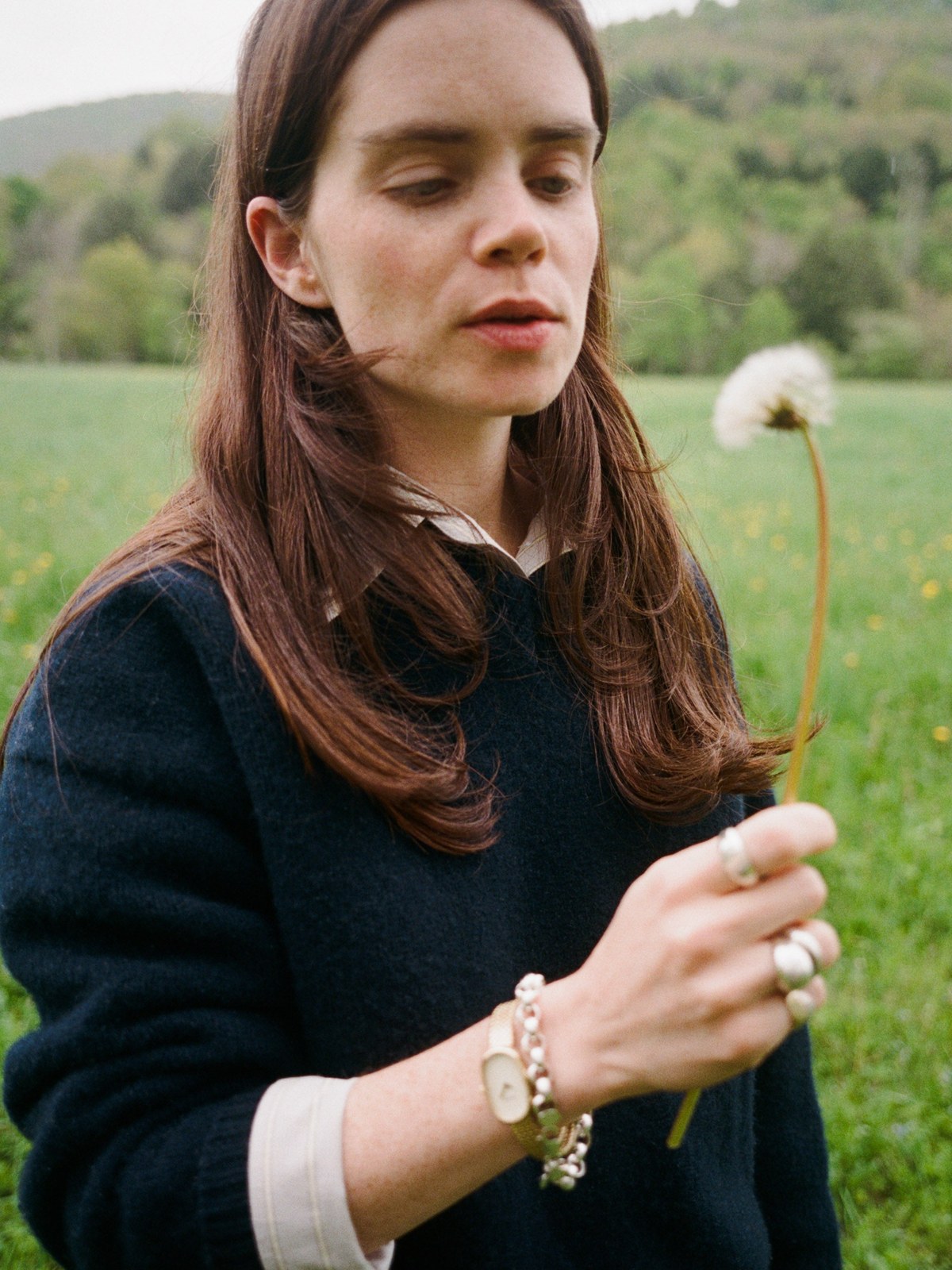 Woman in a navy sweater wearing a gold watch and holding a small flower