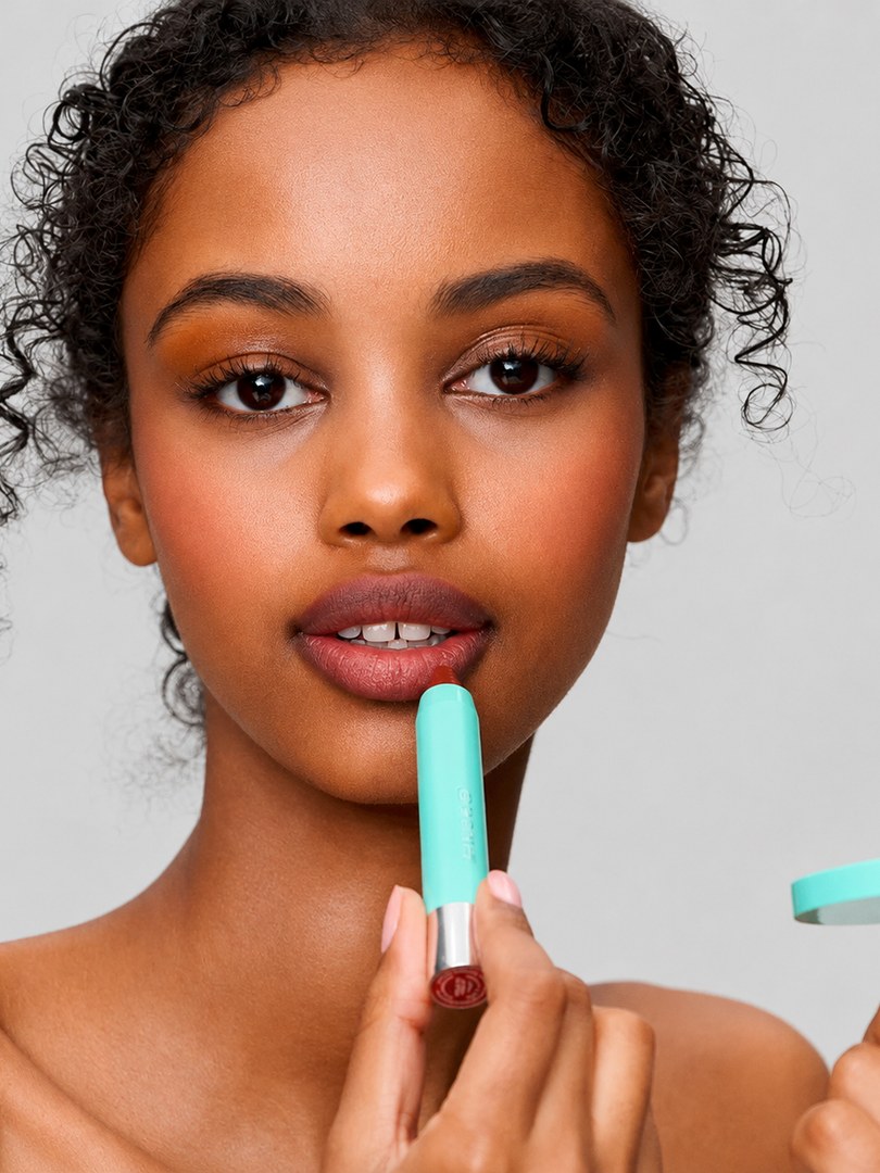 Model applying a mint SWEED lip color in a bright studio portrait