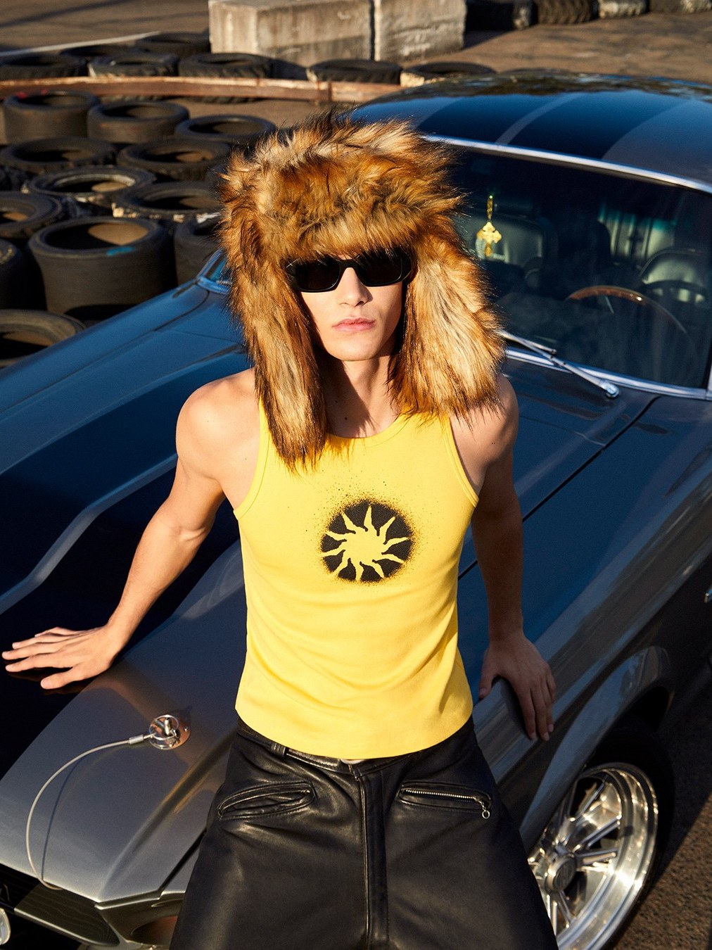 Model wearing sunglasses beside a vintage car.