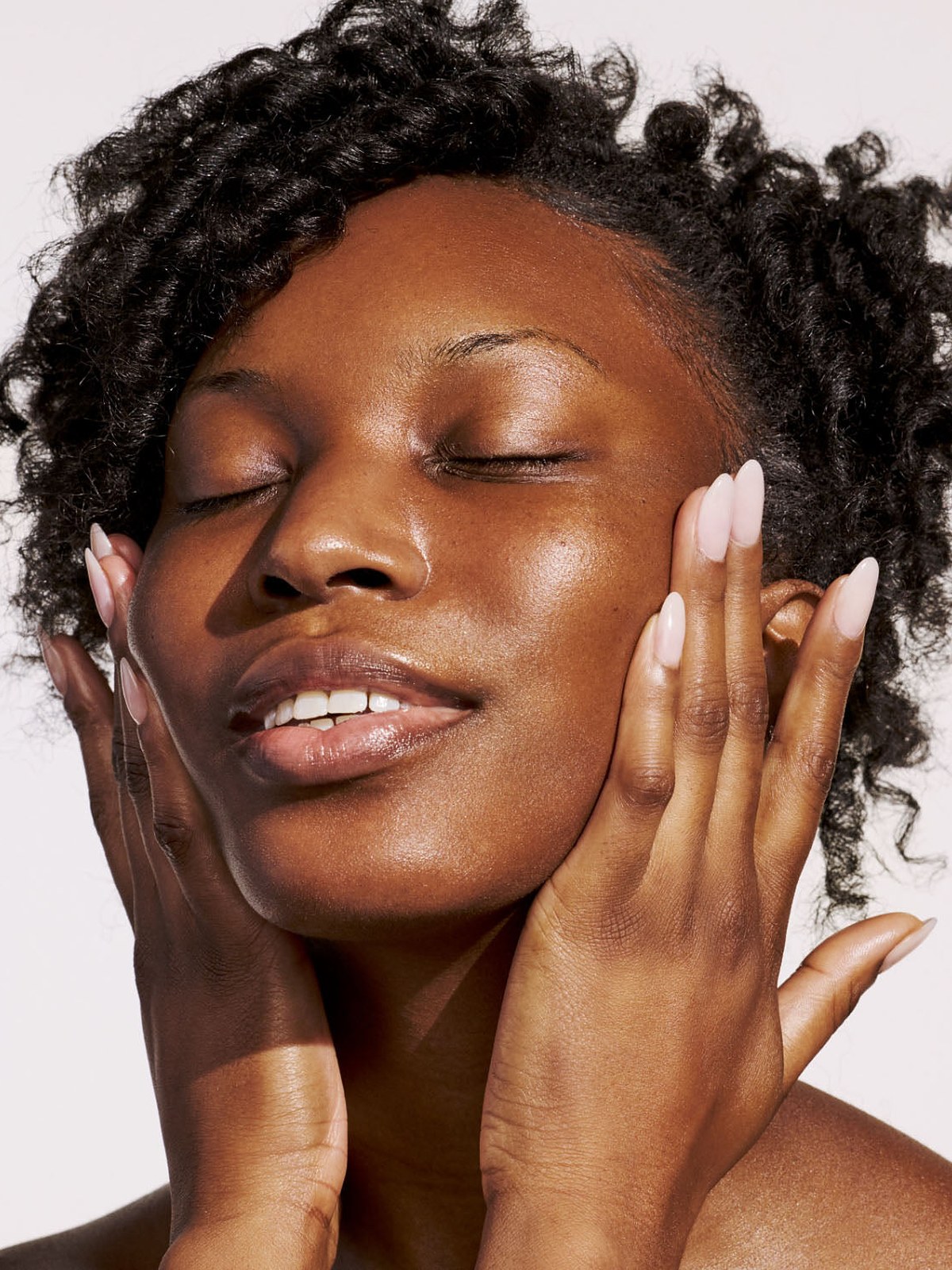 Model with curly hair and dewy skin touching her face