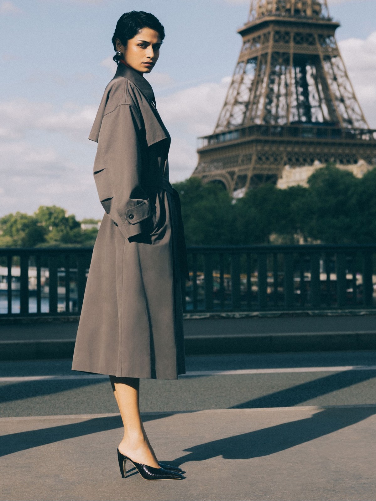 Woman in a taupe trench and black pointed pumps with the Eiffel Tower behind her