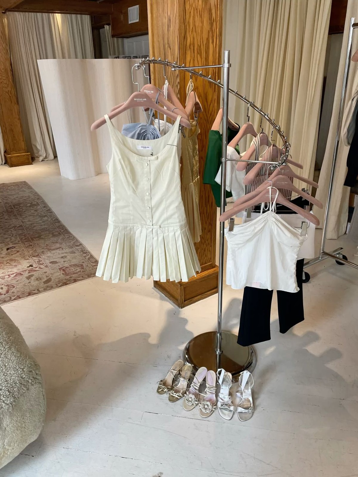 A white dress and blouses on a rack with sandals below