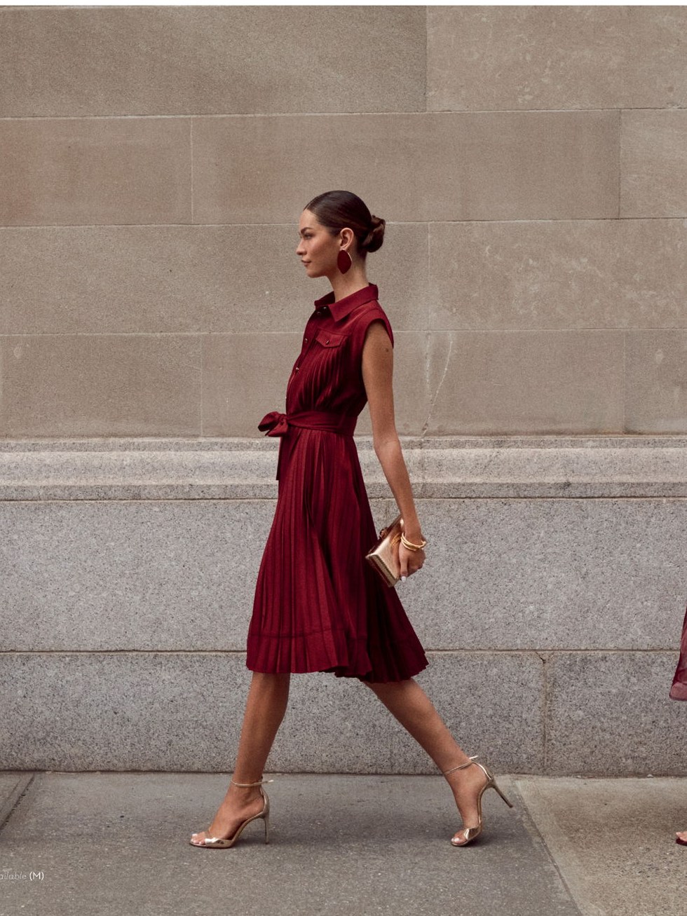 Model walking in a burgundy dress against a stone city wall
