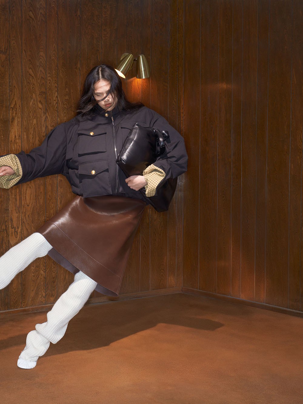 Model in a dark jacket and leather skirt in a wood-paneled room
