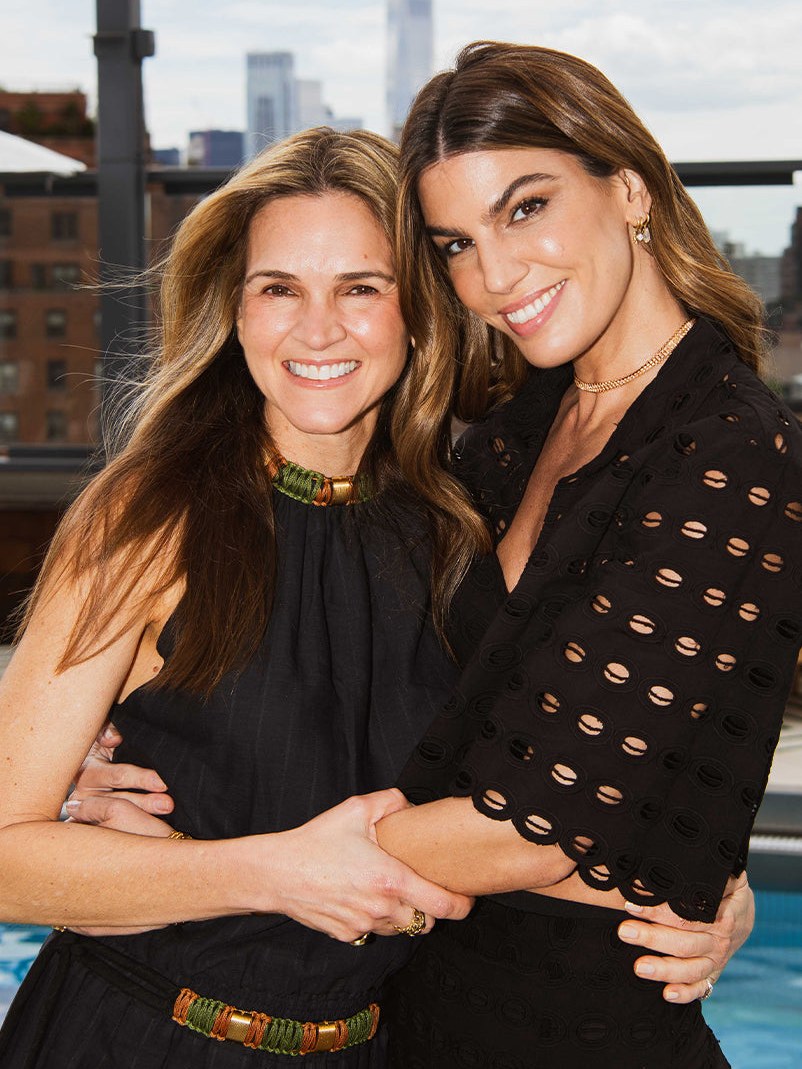 Two women in black resort outfits beside a rooftop pool