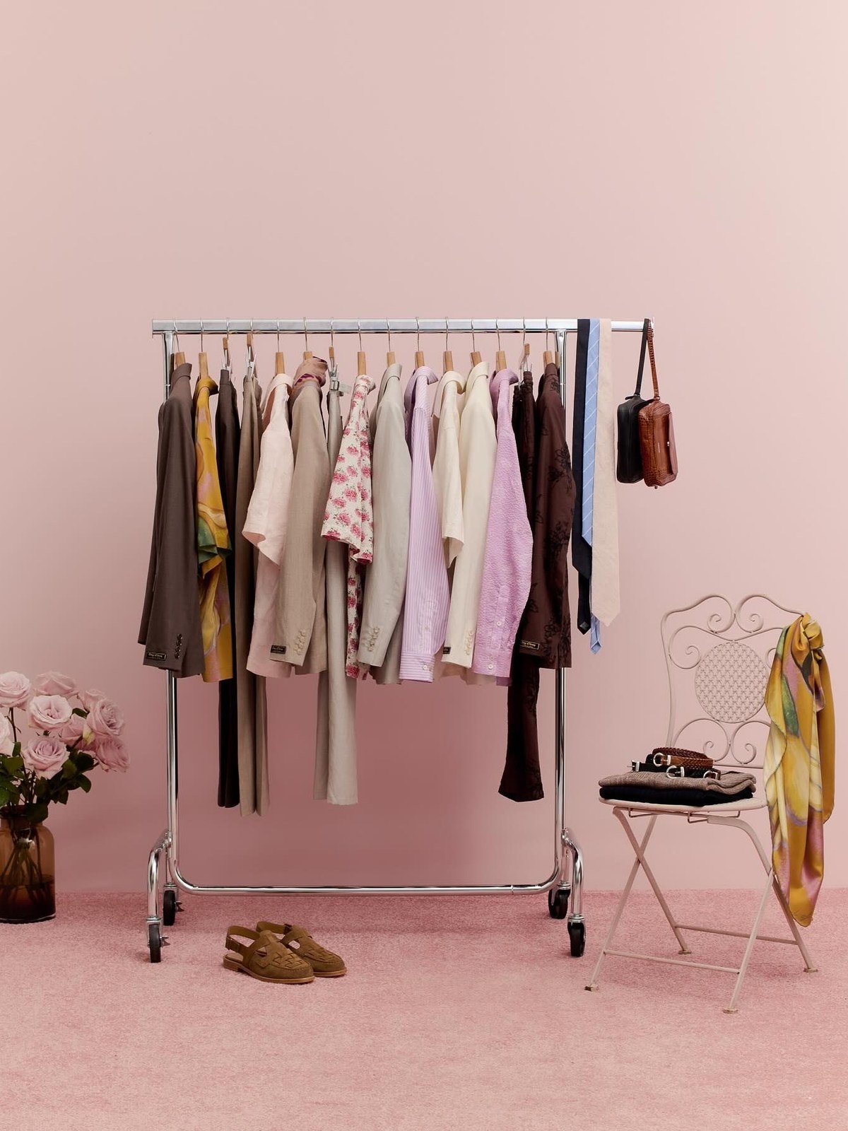 A pastel rail of clothes against a pink wall with a chair beside it