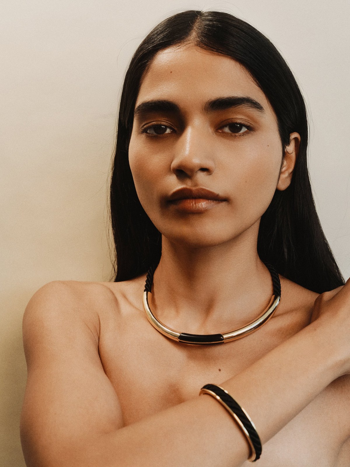 Model in a gold collar necklace and cuff bracelet with arms crossed