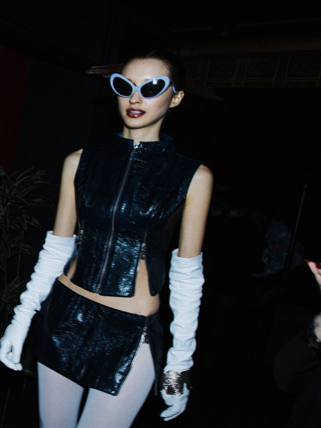 Model in a black sleeveless look and long white gloves at night