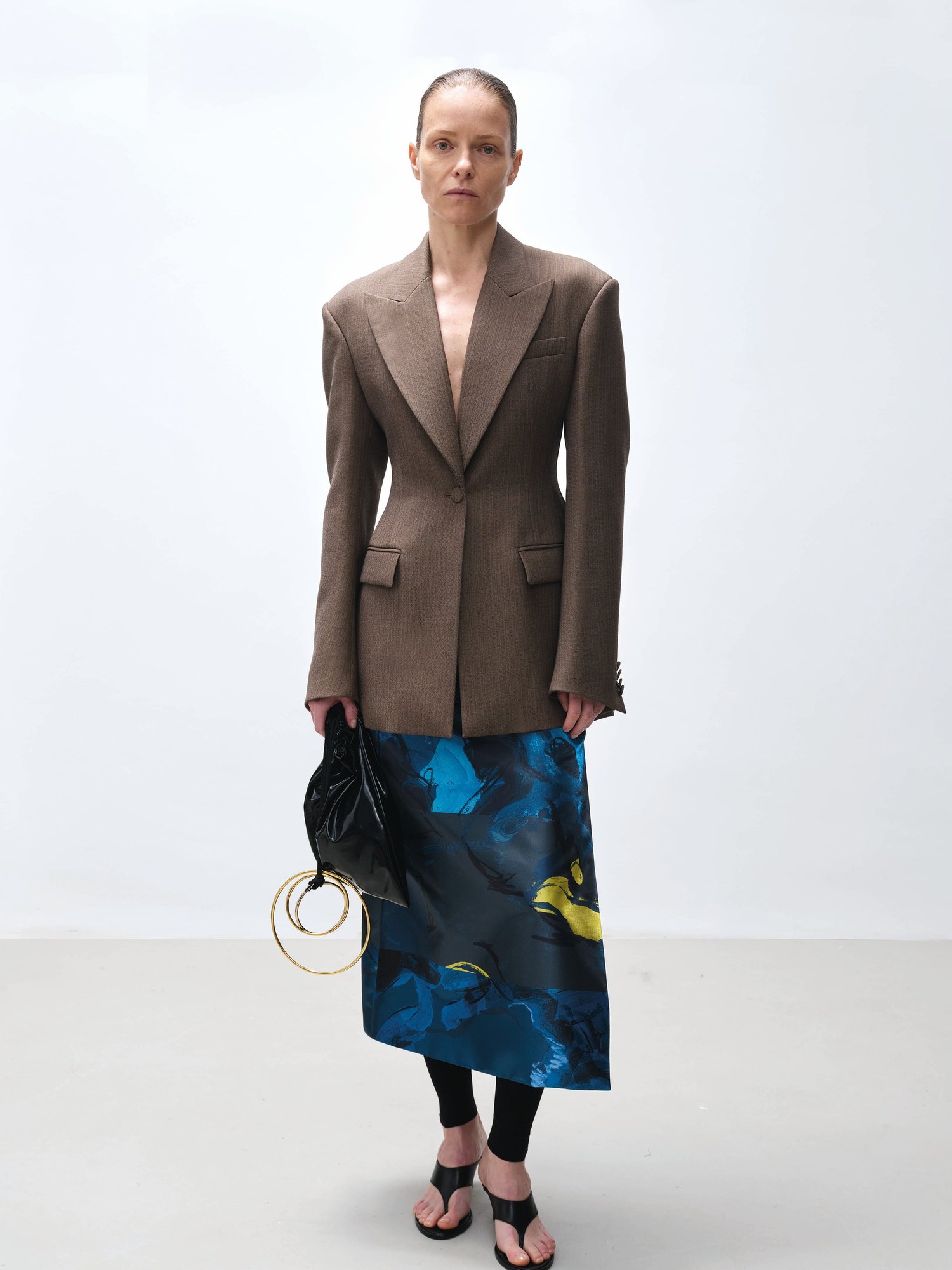Model in a brown tailored blazer over a blue printed skirt with a black bag