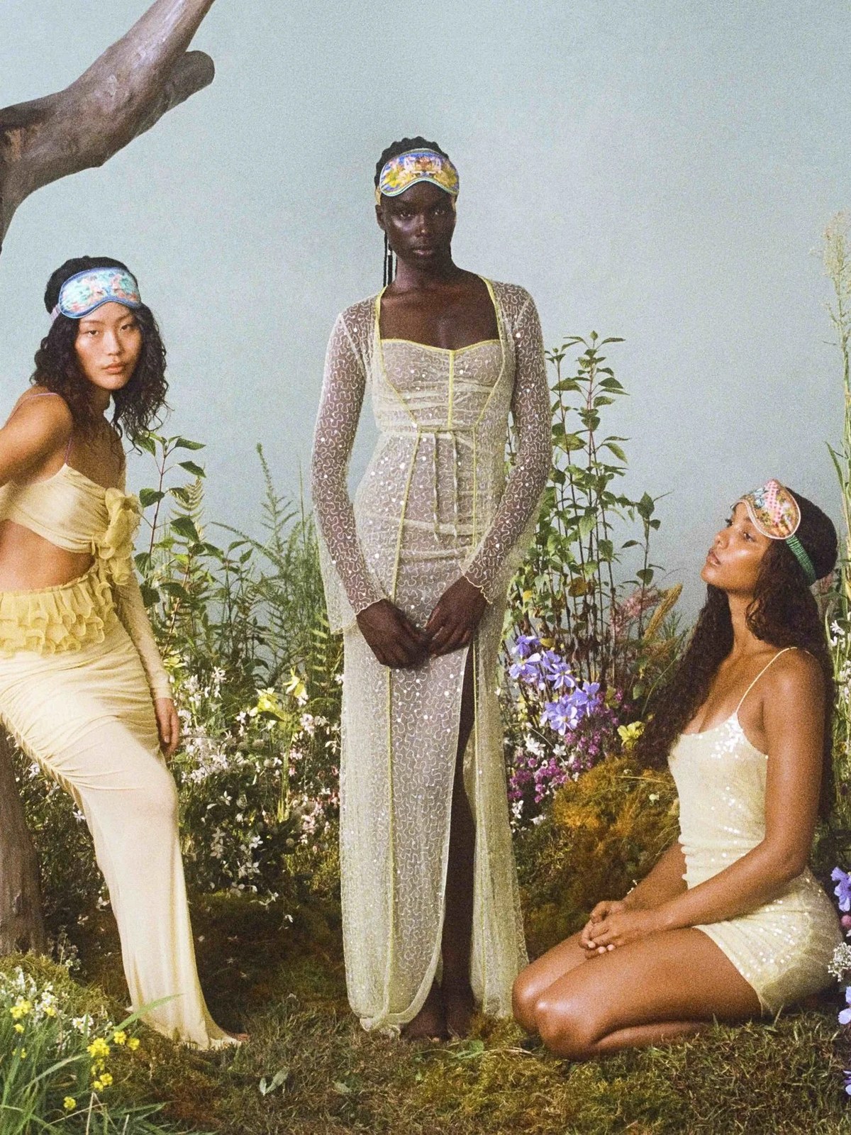 Three models wearing printed sleep masks among flowers and greenery