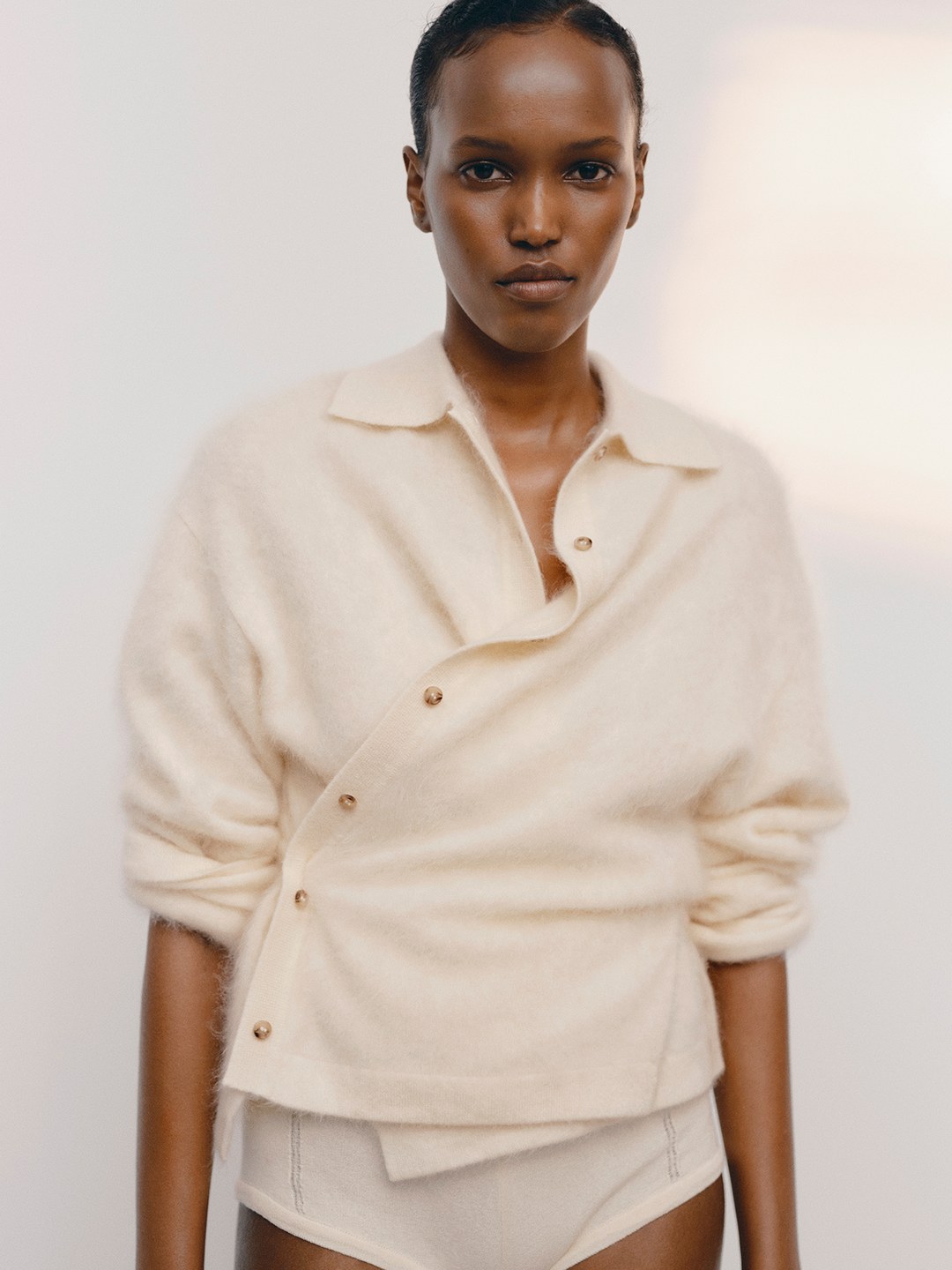 Side portrait of a model in a cream draped top against a pale studio background