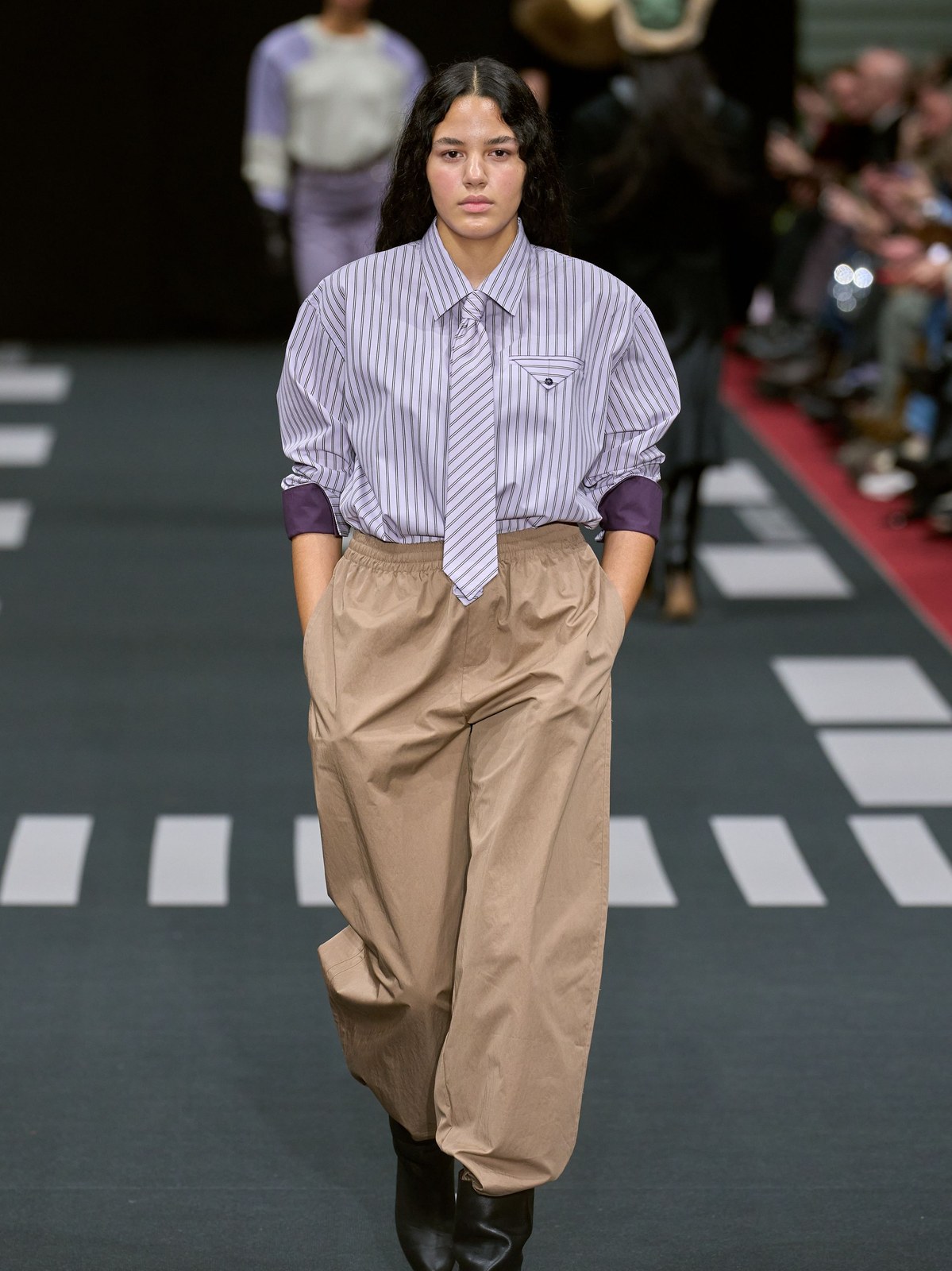 Runway model in a striped button shirt and relaxed tan trousers