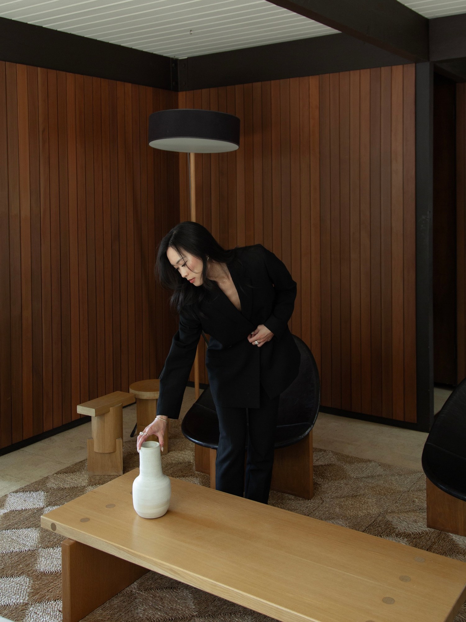 Woman in a black suit leaning over a low wooden table in a wood paneled room