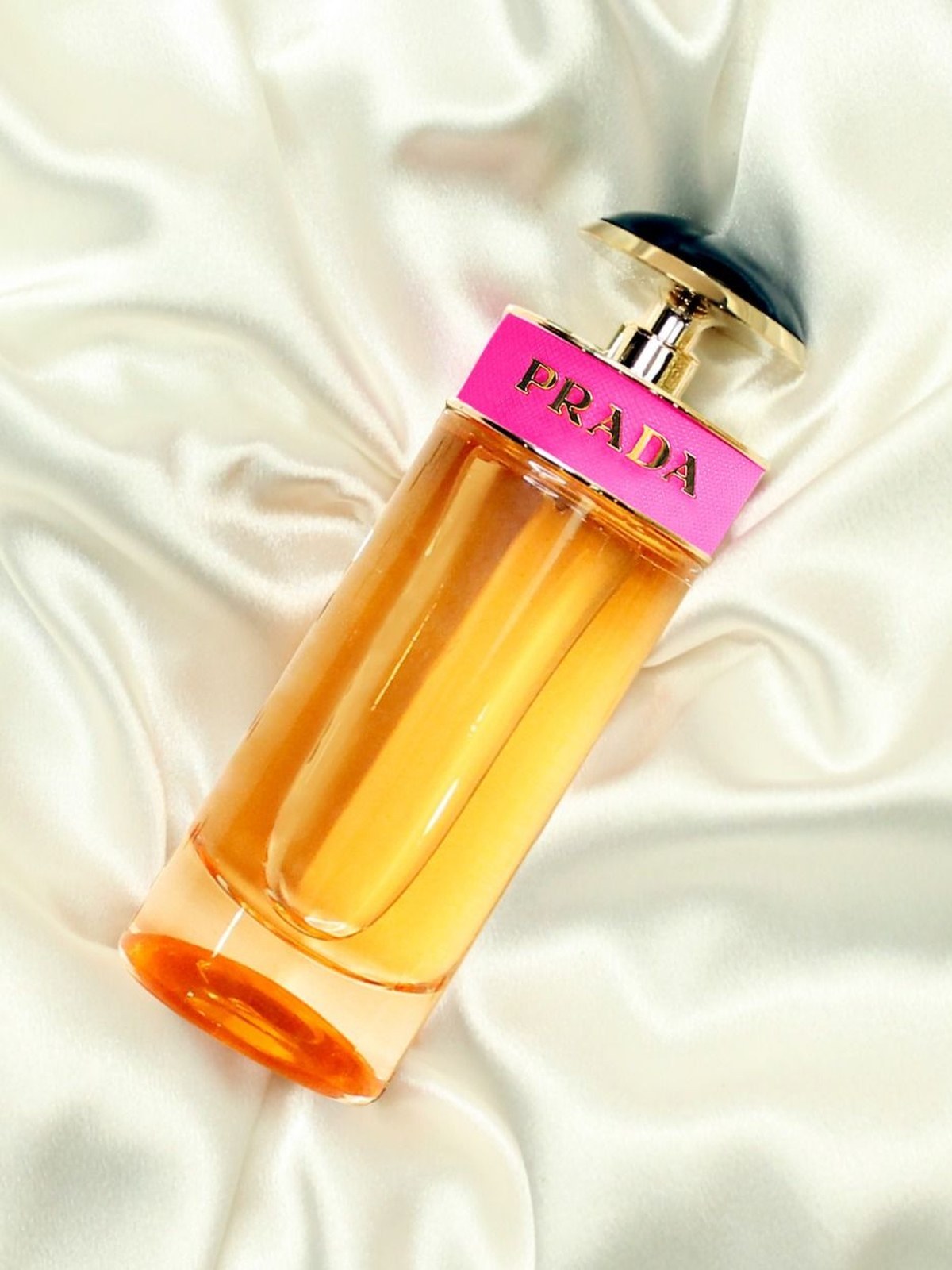 Prada Candy perfume bottle with an amber liquid and a pink band lying on cream satin