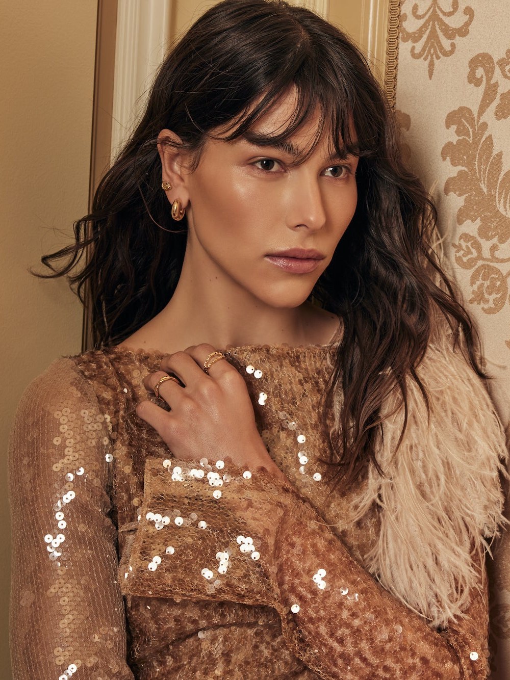 Model in a sequined brown top and feathered wrap with gold hoops and rings