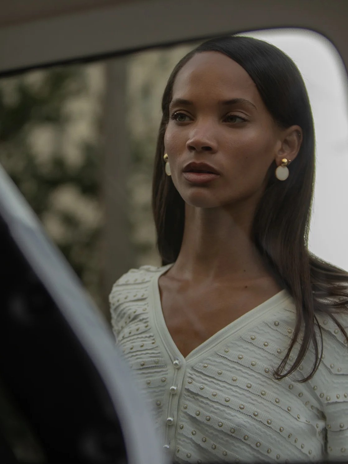 Model in a white embellished cardigan beside a car