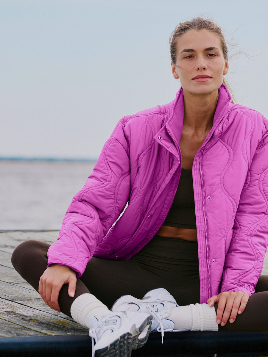 Woman in a magenta jacket sitting on a waterfront dock