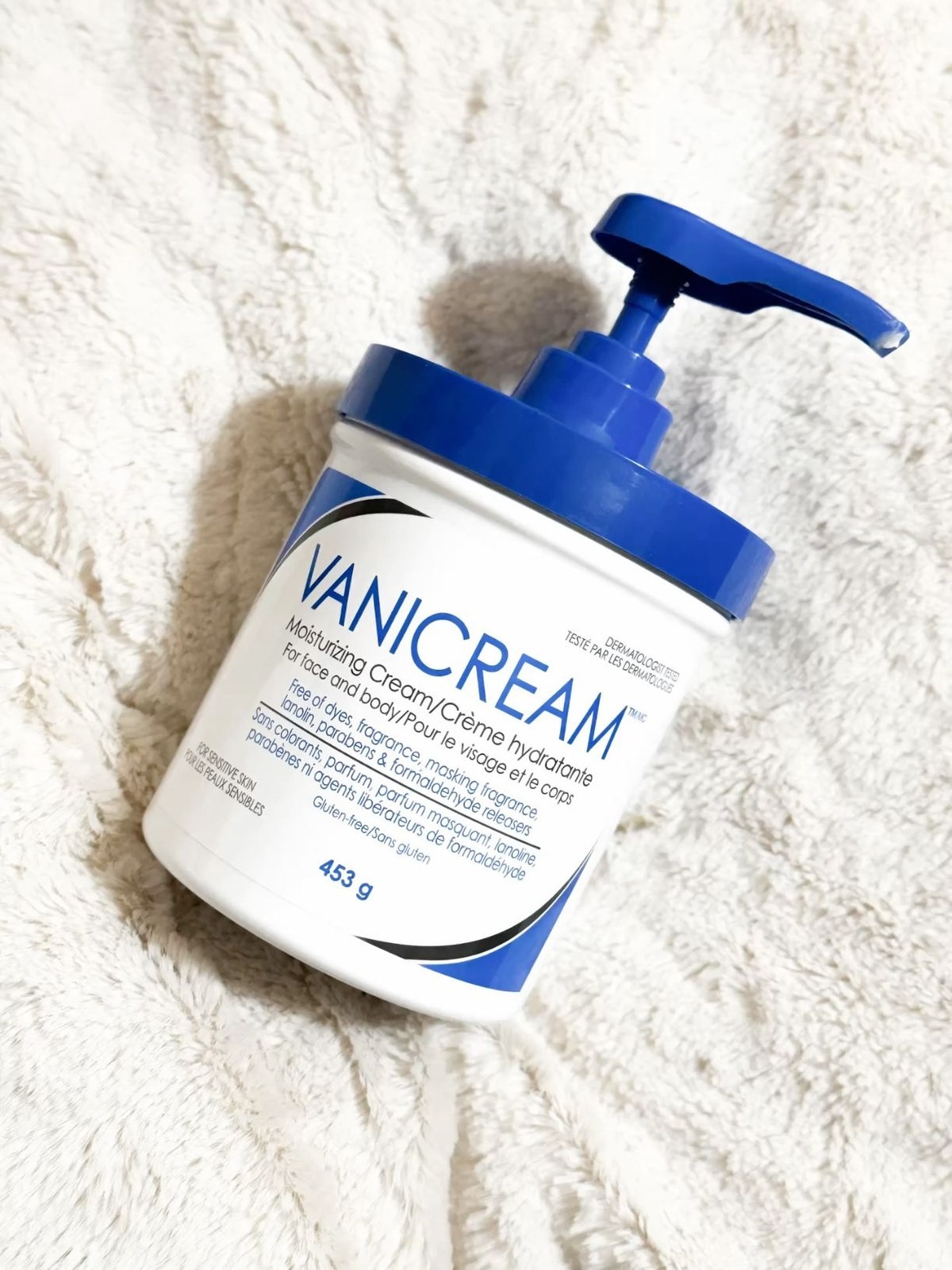 Vanicream Moisturizing Cream pump jar with blue lid resting on a cream faux fur blanket