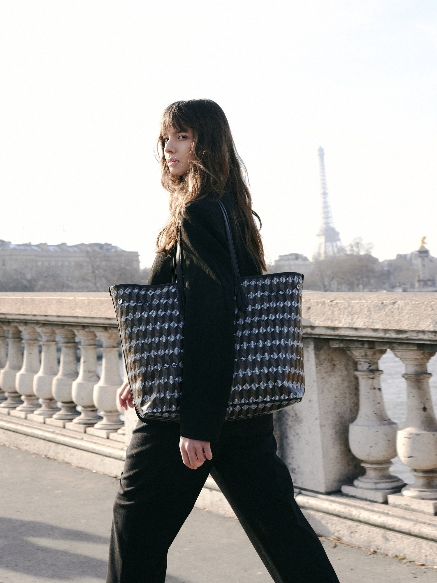 Model in black carrying the monogram tote on a Paris bridge with the Eiffel Tower behind