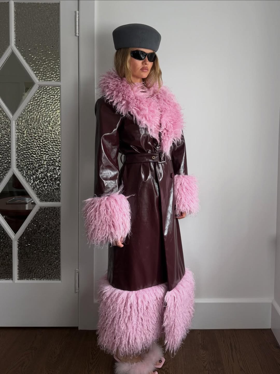 Model in a plum coat with pink textured trim and a sculptural gray hat