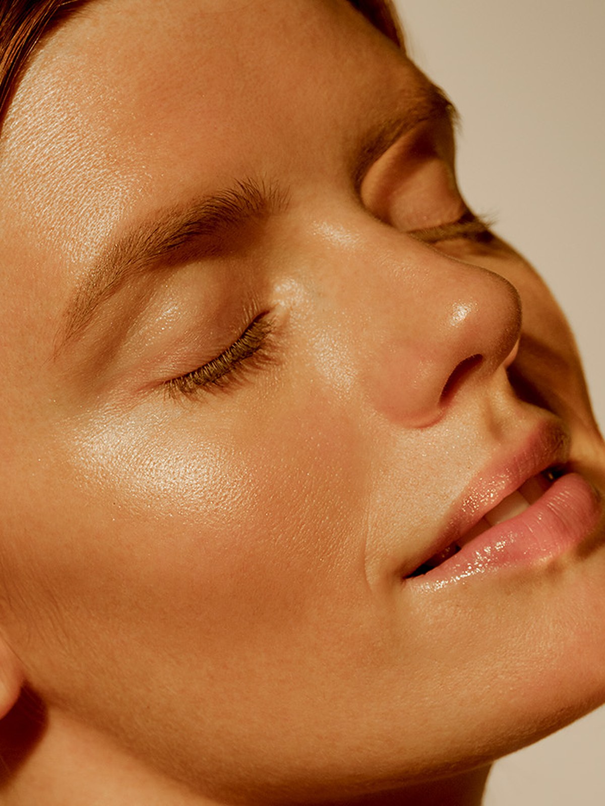 Model with glowing skin and closed eyes holding an open bronzer compact