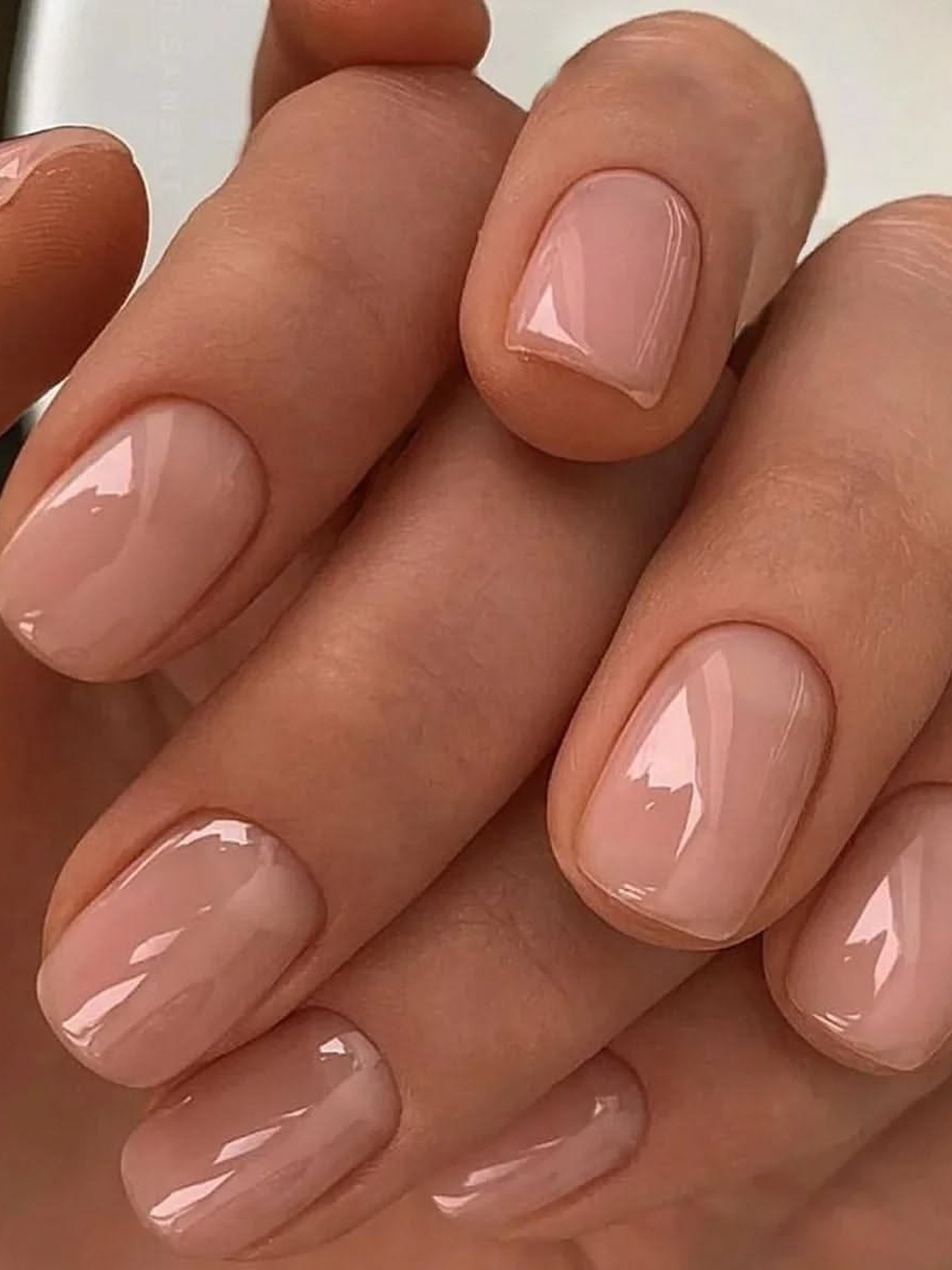 Short rounded nails in a glossy nude-pink polish with bright reflections