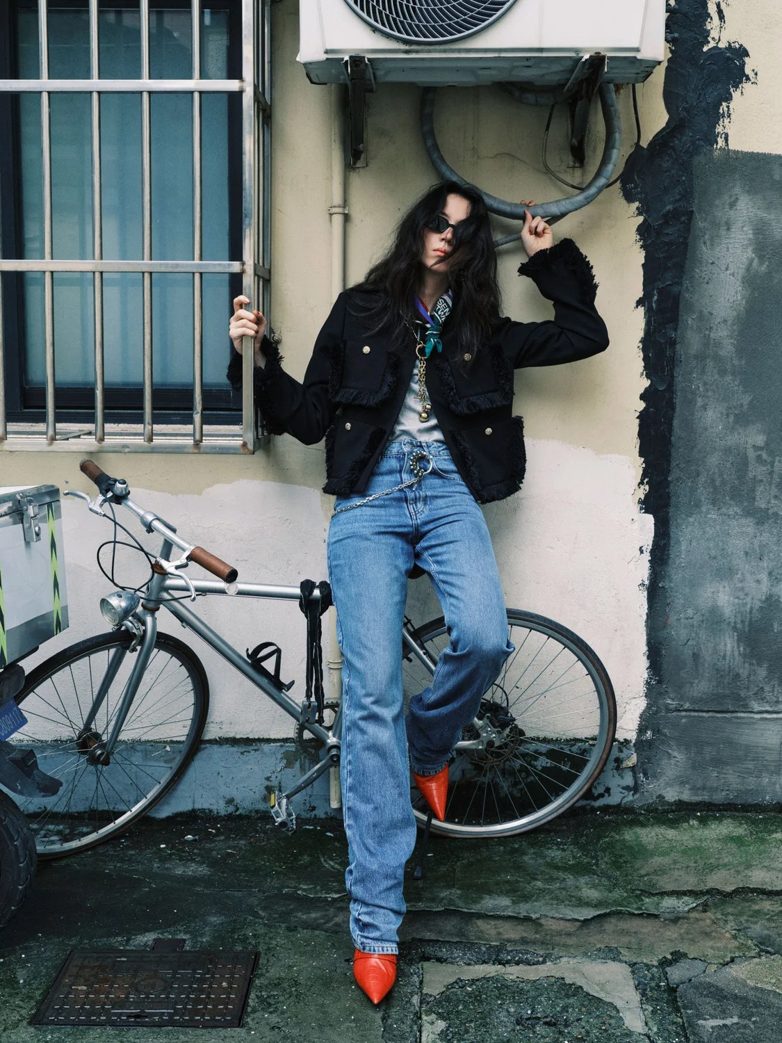 Model in a black jacket and jeans leaning beside a bicycle