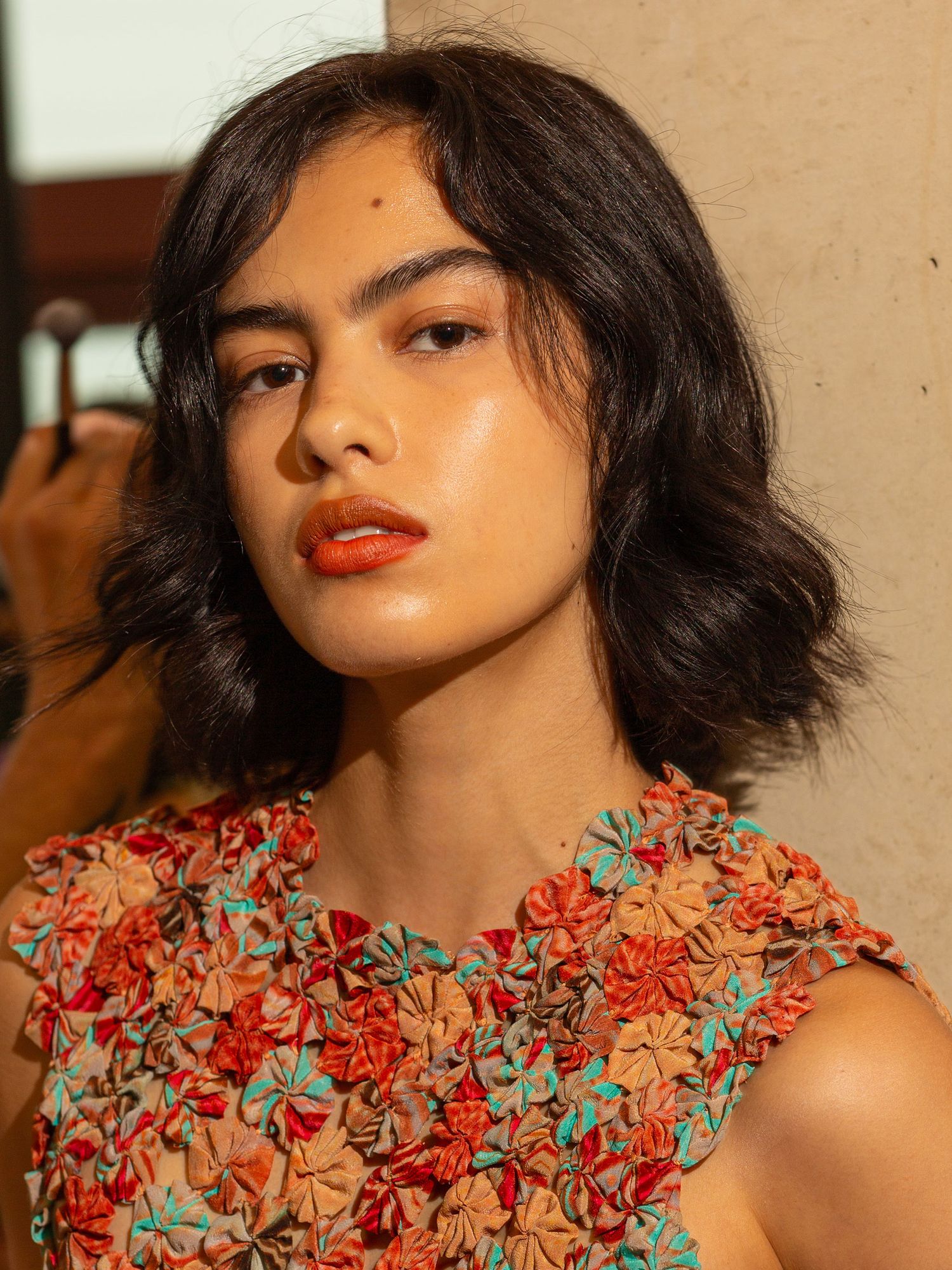 Backstage portrait of a model with a dark bob and orange lip in a floral top