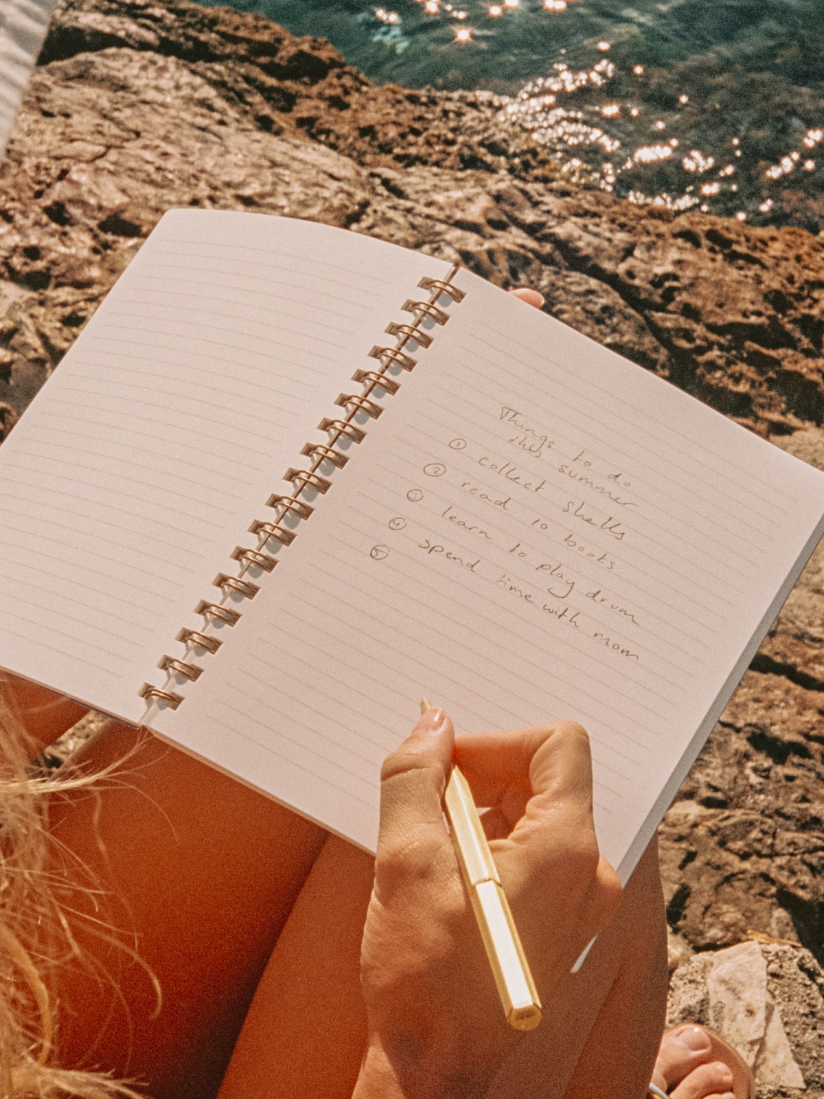 Hand writing in a Papier notebook on a rocky shore
