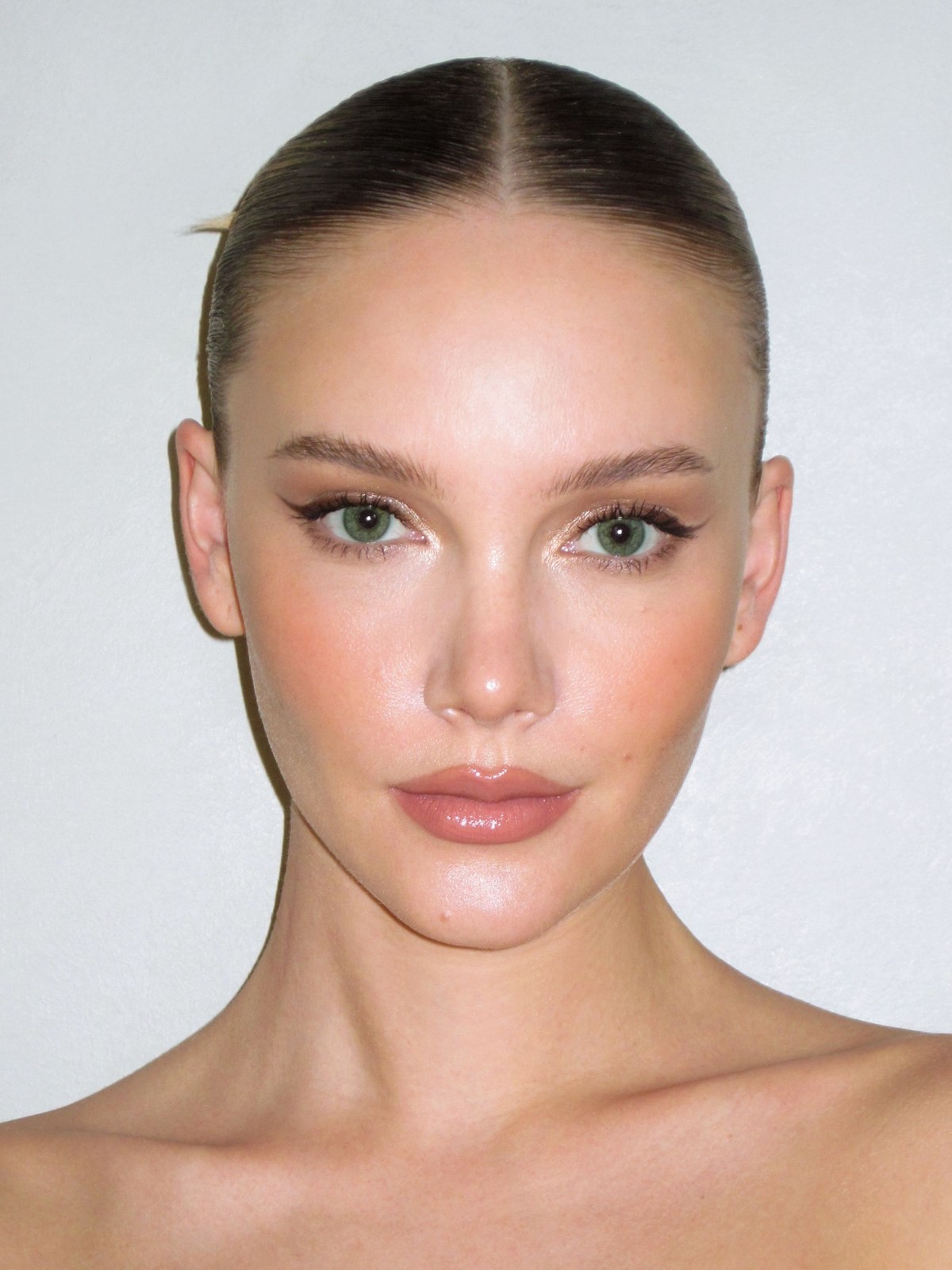 Close up of model's face with sleek center part, winged eyeliner and glossy lips