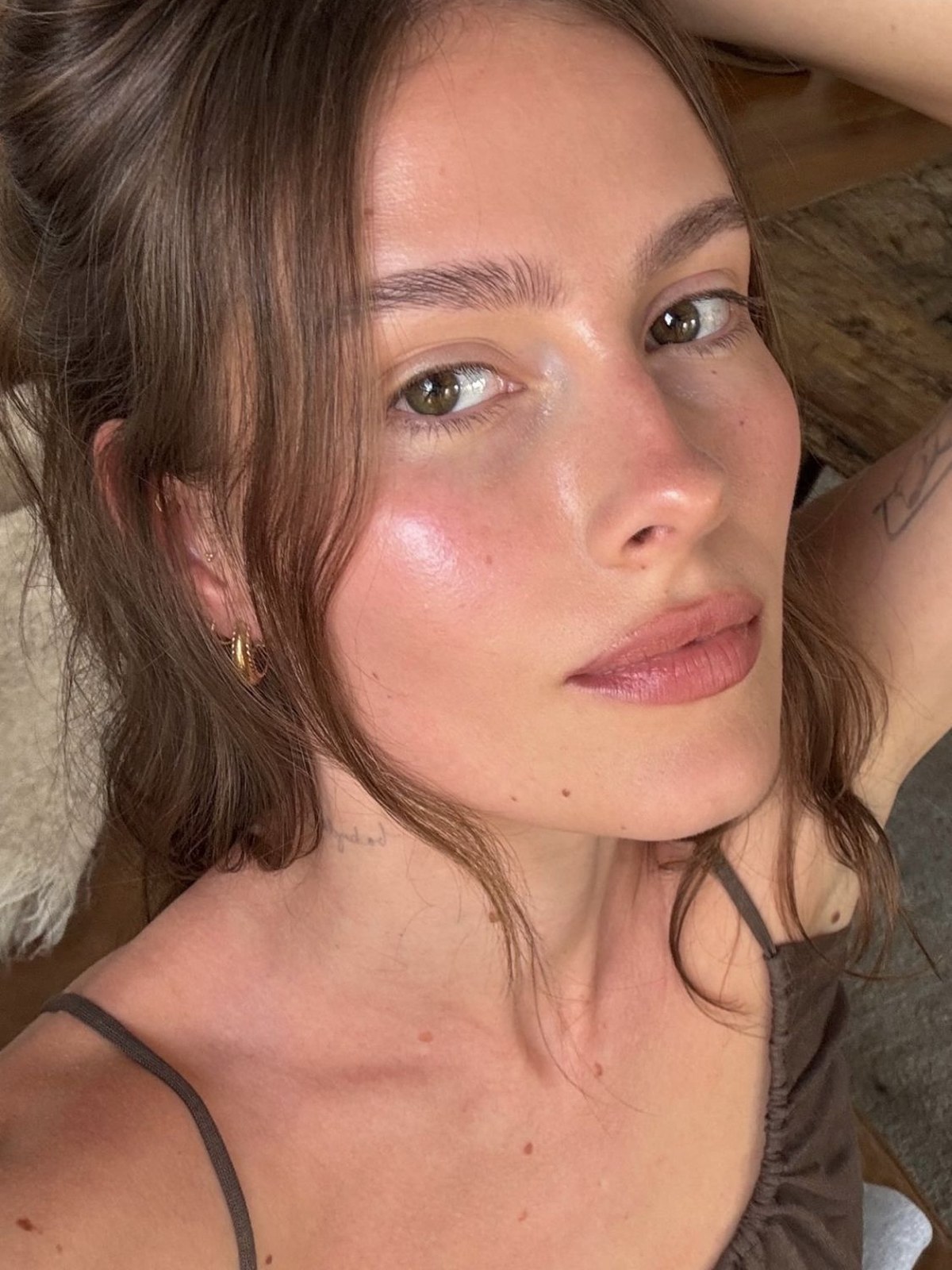 Selfie of a woman with brown hair pinned up, a luminous glow on her cheek, natural freckles and a pink-brown lip