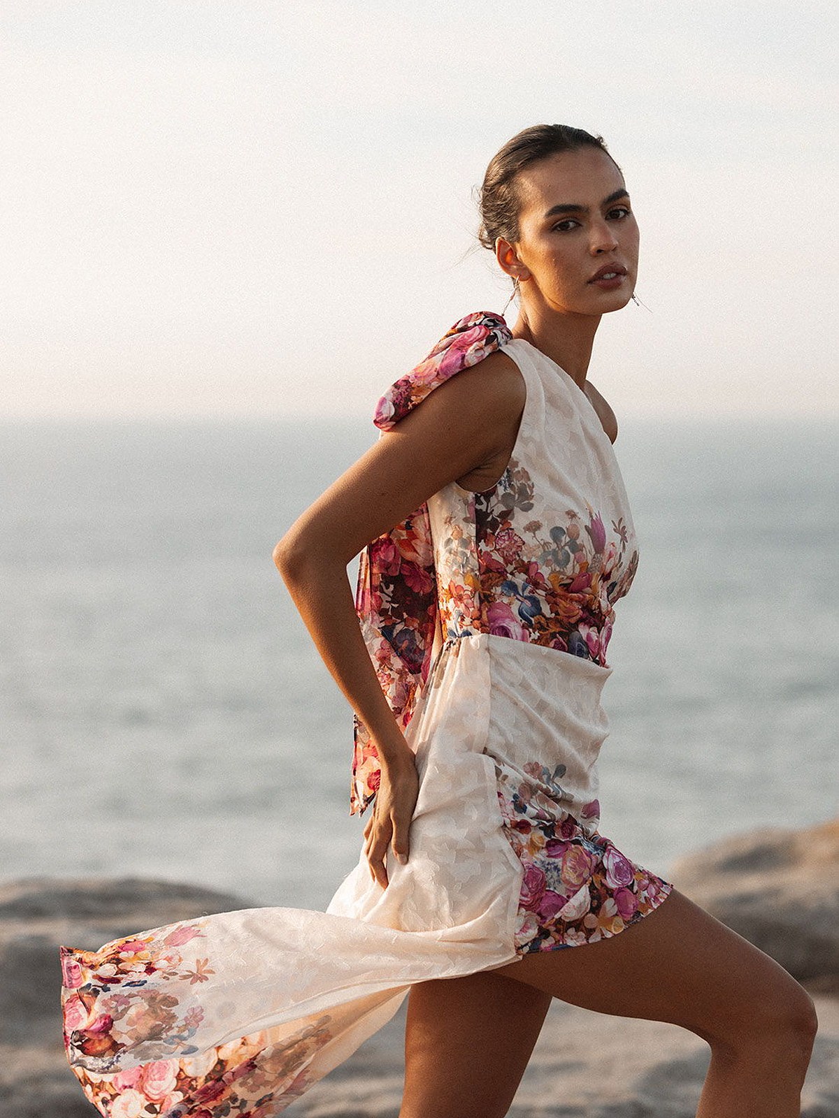 Model in a floral print dress with a flowing skirt on a beach