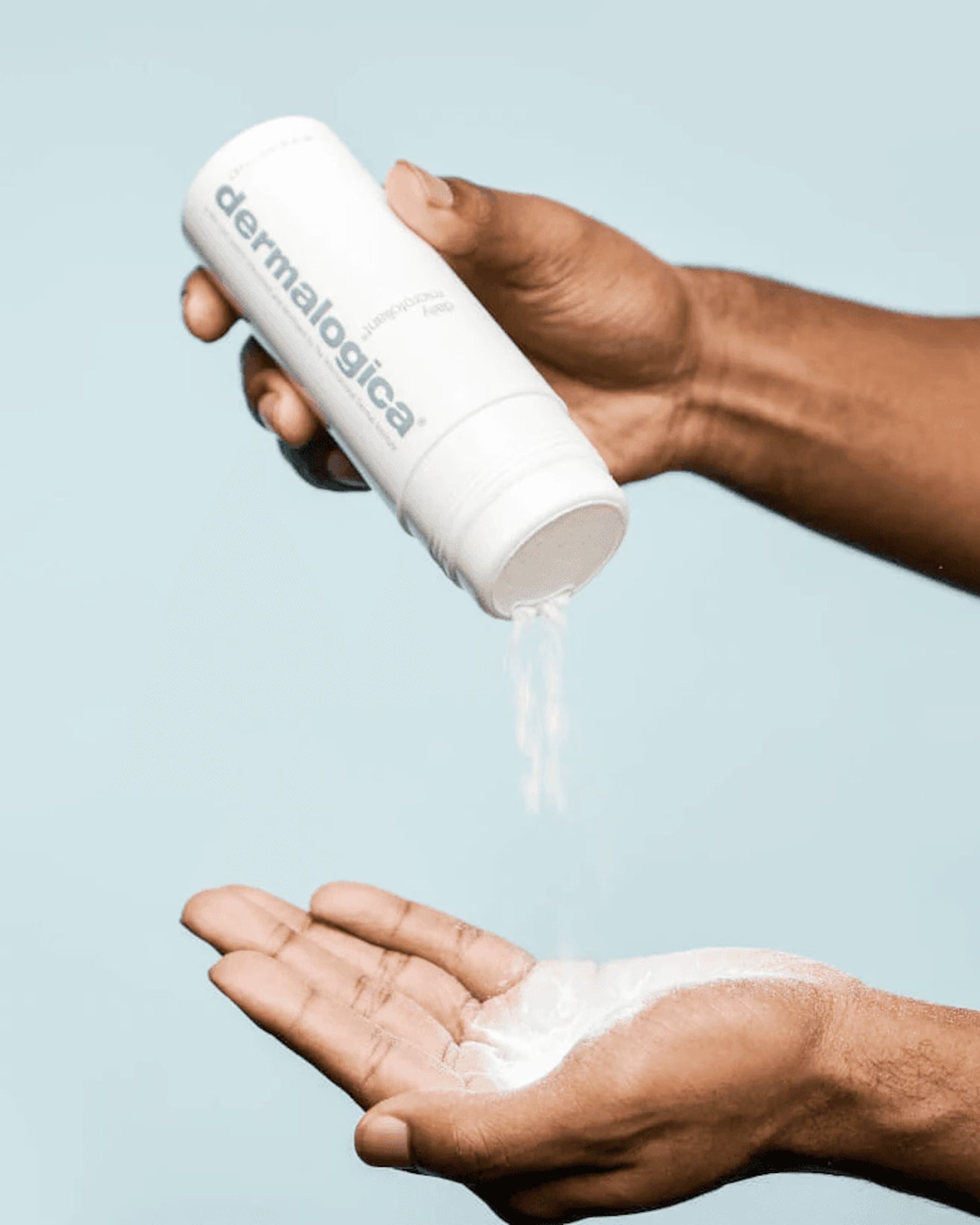 Two hands against a pale blue background, one pouring Dermalogica Daily Microfoliant powder into the open palm of the other