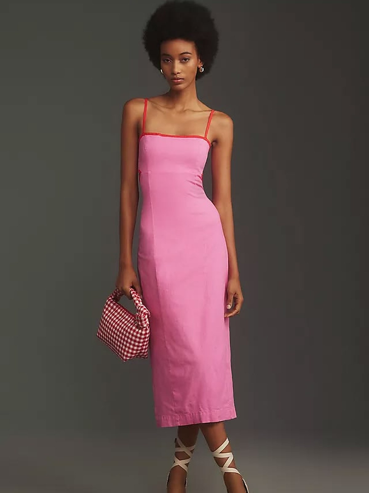 Model in a pink strapless midi dress with a striped clutch against a grey backdrop