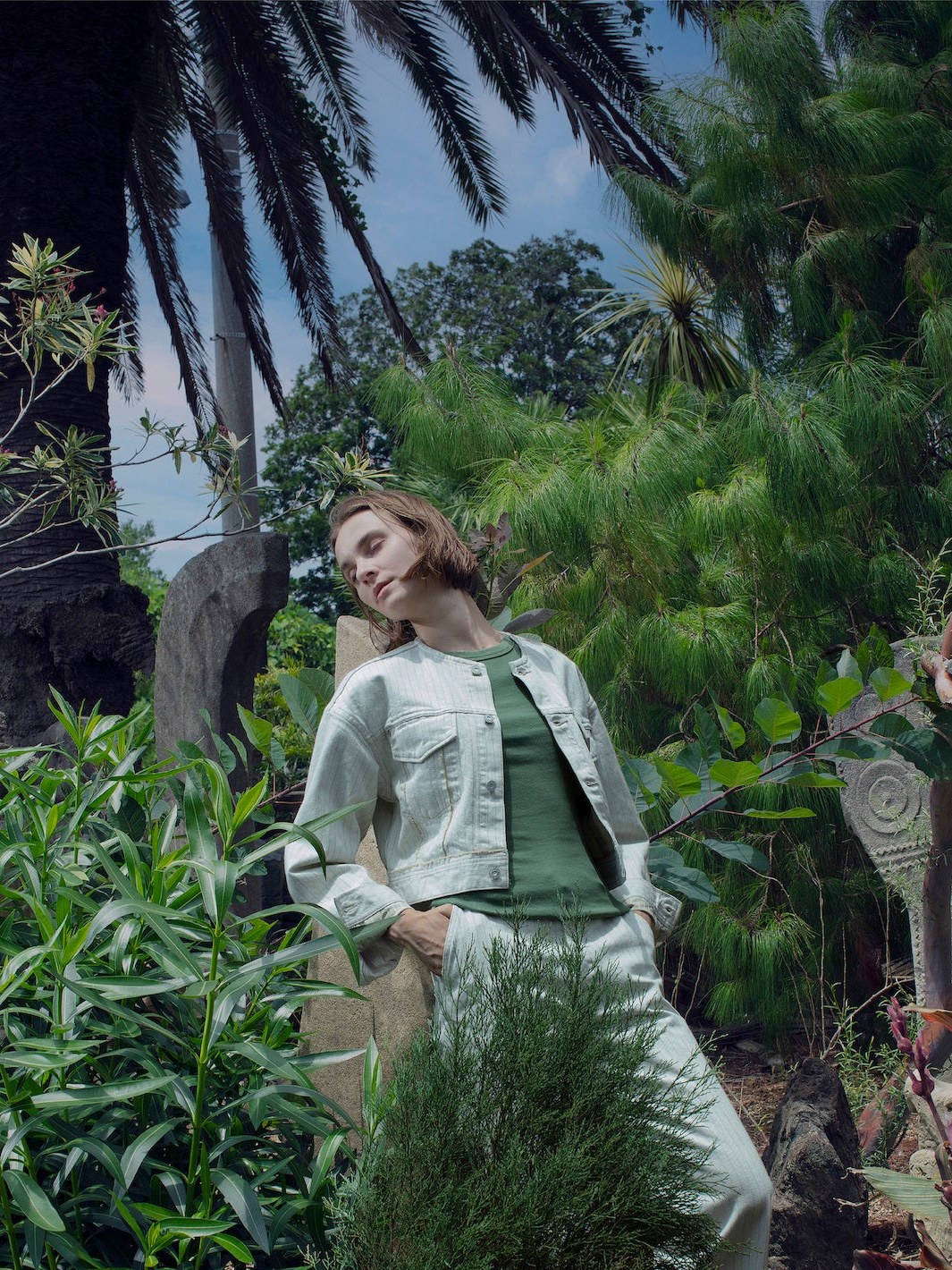Model in a pale denim jacket and trousers among tropical plants