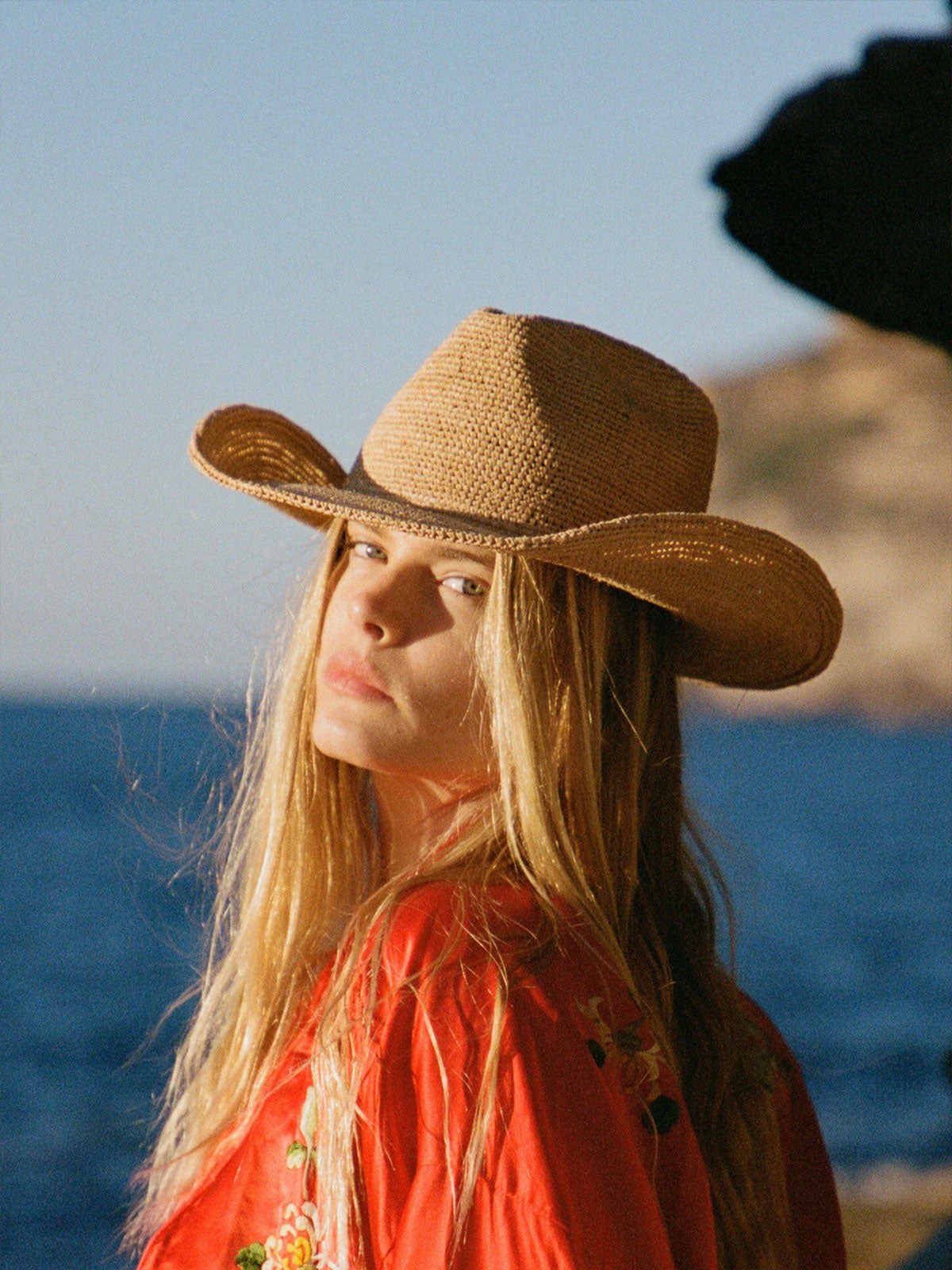 Model in a wide raffia fedora and red shirt by the sea