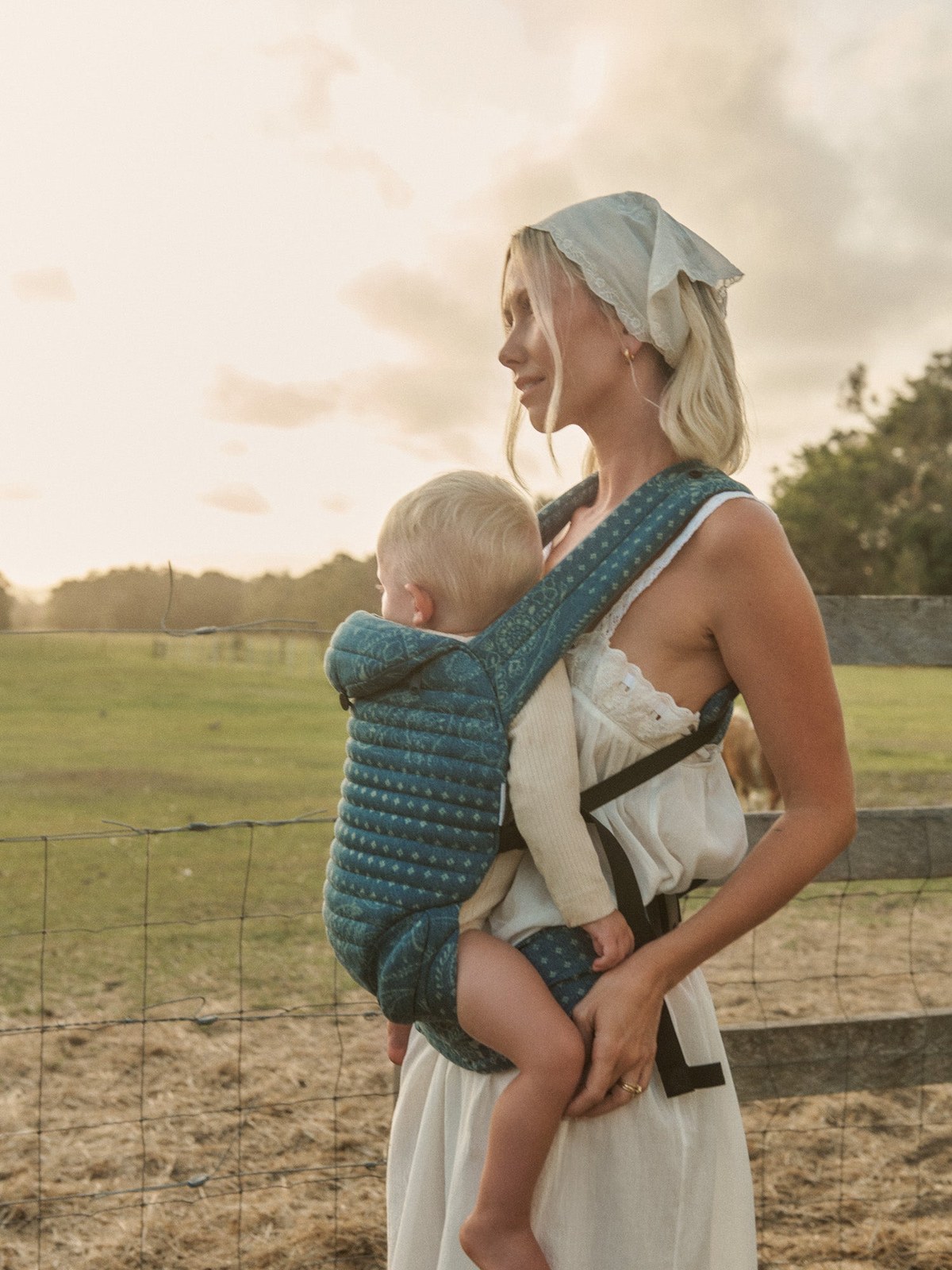 Mother Lisa Green carrying her baby in a blue patterned carrier while standing in a field.