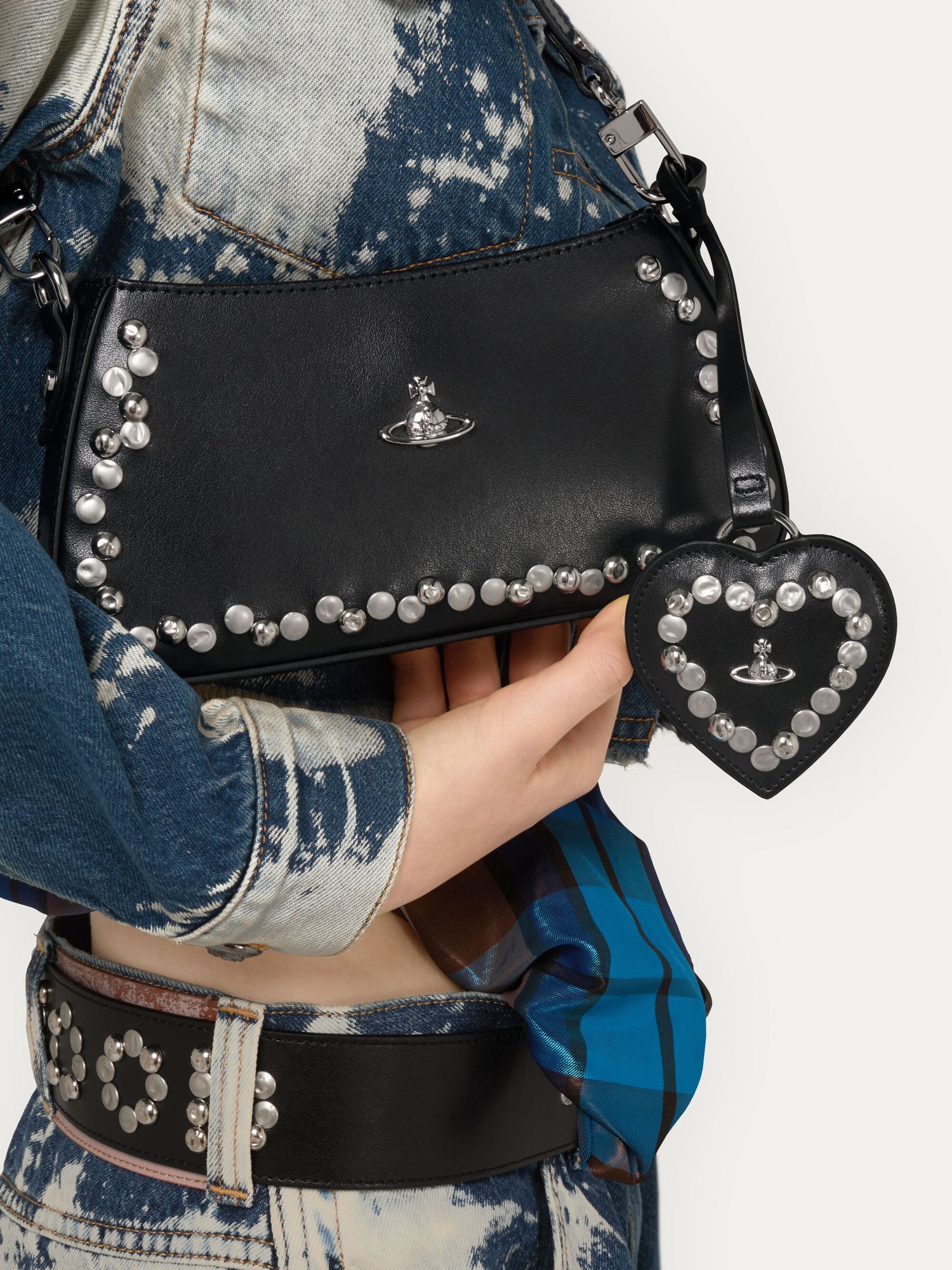 Studded black shoulder bag with heart charm worn with acid wash denim