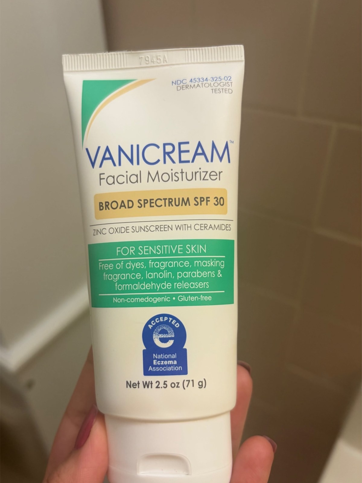 Hand holding a tube of Vanicream Facial Moisturizer with Broad Spectrum SPF 30 in a bathroom